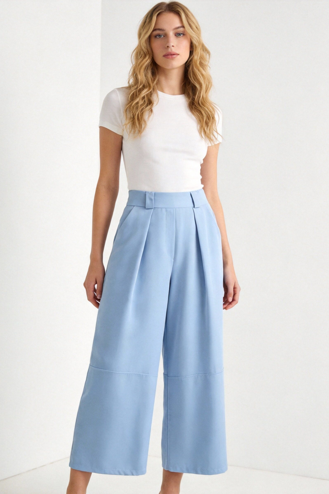 Femme debout dans un pantalon court plissé taille haute ceinture élastique à poches, mettant en avant un style chic et moderne. Pantalon plissé femme.