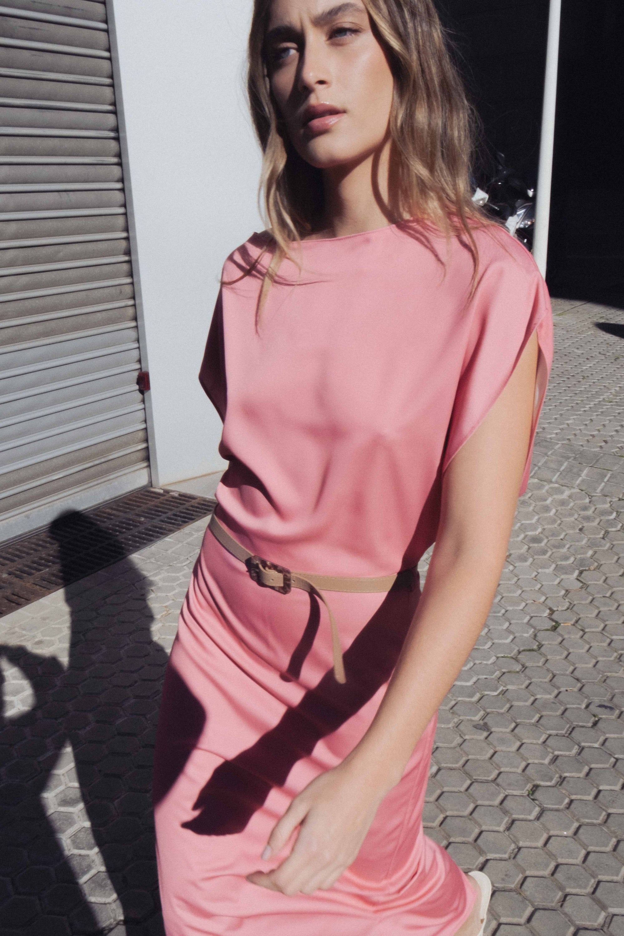 Femme marchant avec assurance en robe midi satinée avec ceinture fine couleur rose, montrant un style contemporain.