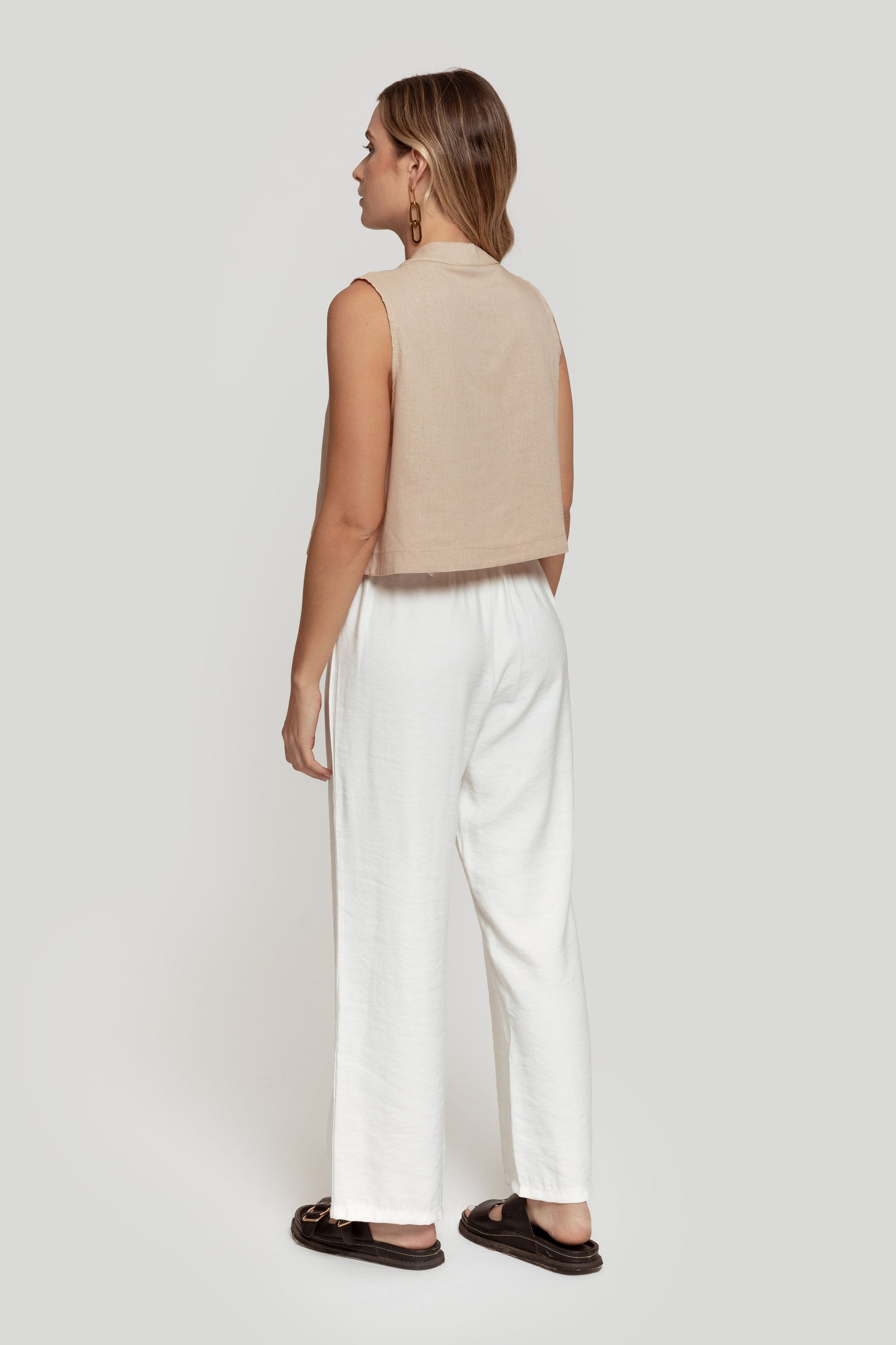 Vue arrière d'une femme avec un top beige, montrant le pantalon paperbag taille haute blanc, parfait pour un style décontracté.