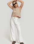 Femme portant un top beige et un pantalon paperbag taille haute fluide taille haute en blanc, mettant en valeur un look décontracté et chic avec le pantalon paperbag taille haute.
