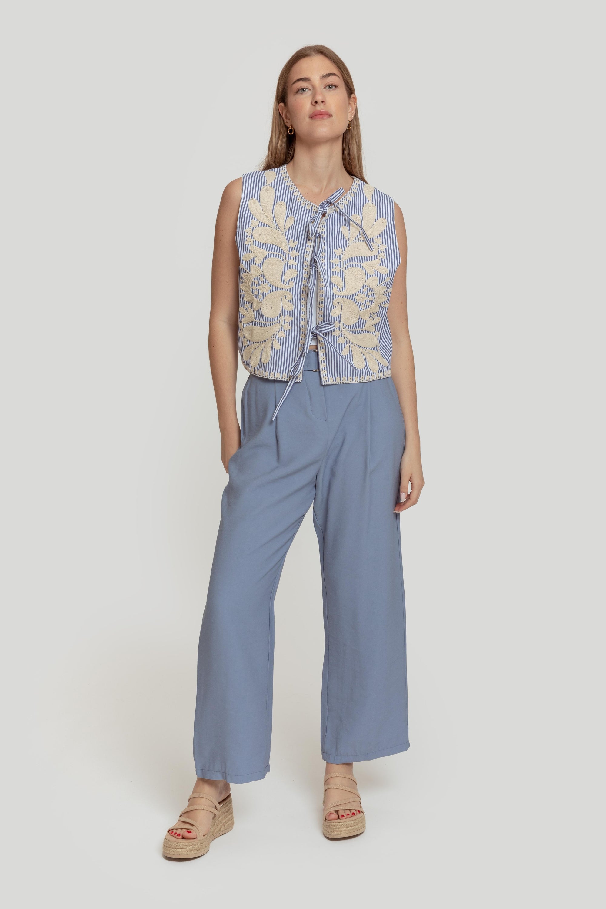 Femme présentant un pantalon paperbag taille haute bleu, associé à un haut à motifs, créant un look estival moderne.