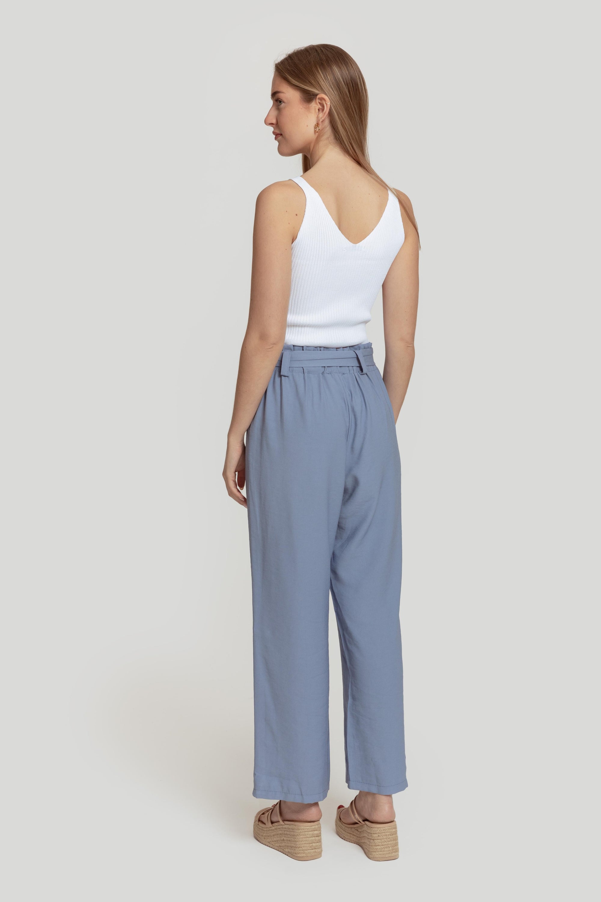 Vue arrière d'une femme en pantalon paperbag taille haute bleu, soulignant la coupe fluide et élégante.