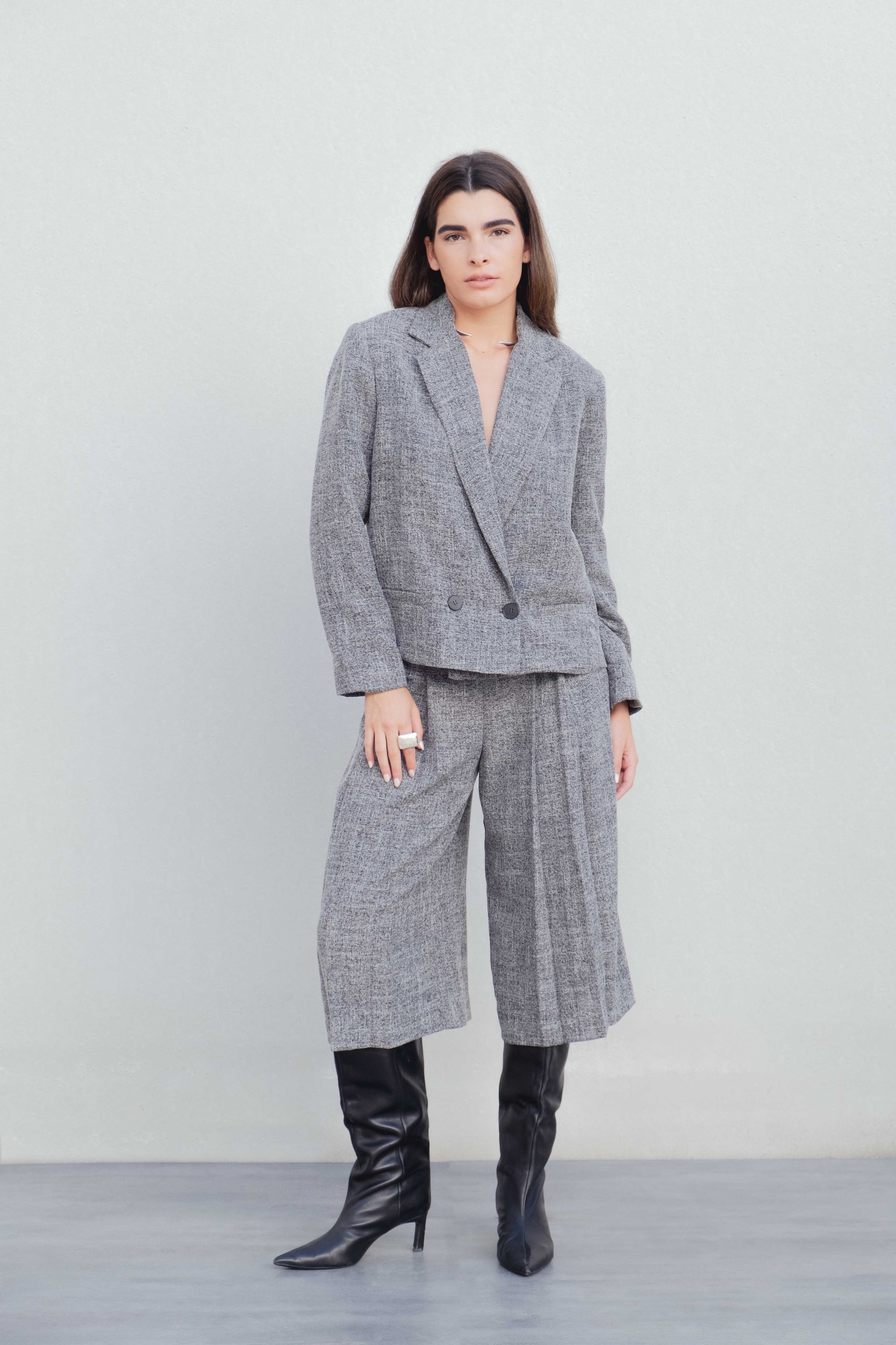 Femme en tenue chic avec un blazer gris et Bermuda gris taille haute à pinces coupe large, se tenant debout pour montrer le design.