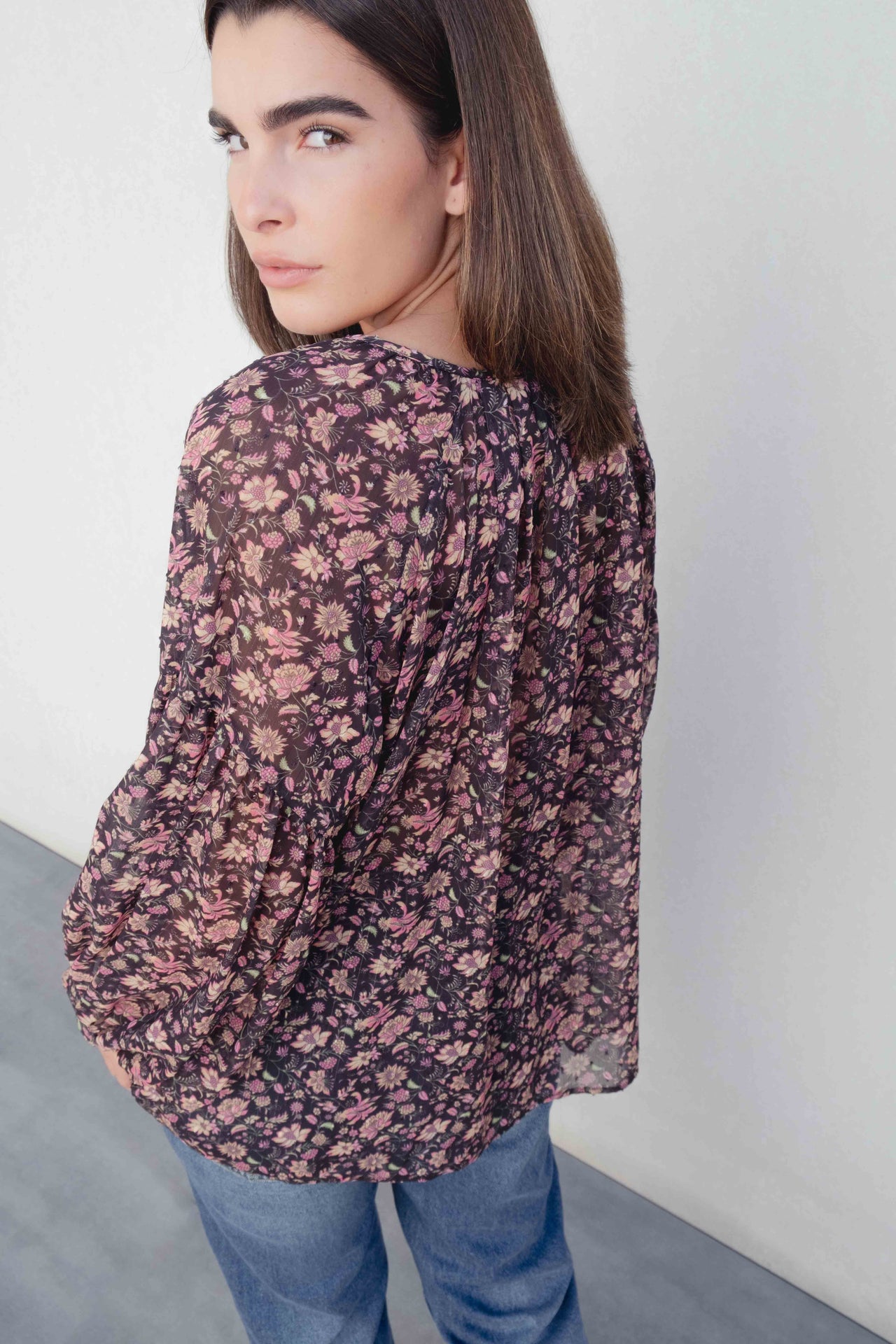 Femme portant une blouse semi-transparente coupe fluide noire voile léger avec imprimé floral, idéale pour un style décontracté. Blouse fleurie femme.