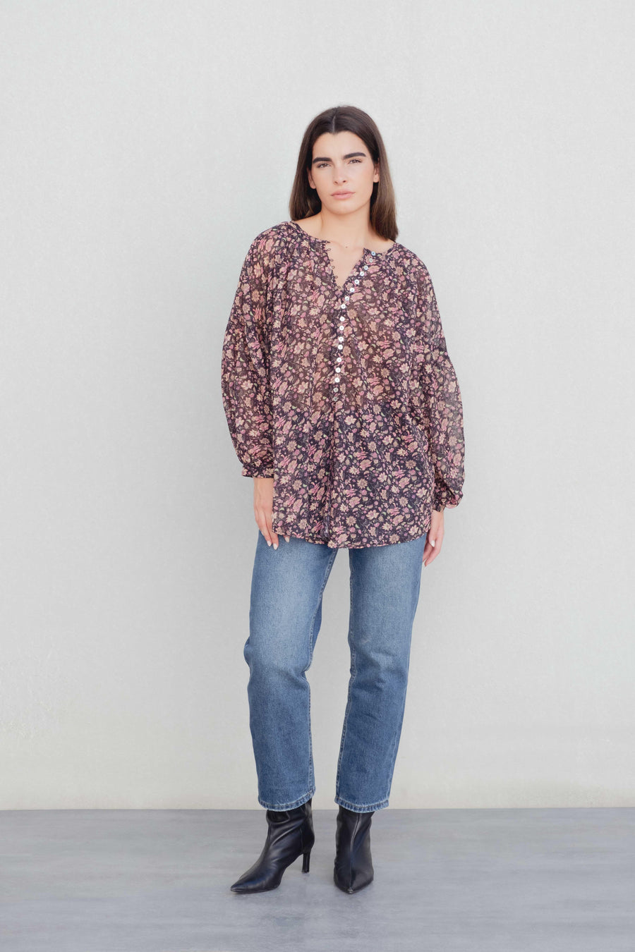 Femme présentant une blouse semi-transparente noire à fleurs, associée à un jean, parfaite pour un look casual. Blouse fleurie femme.