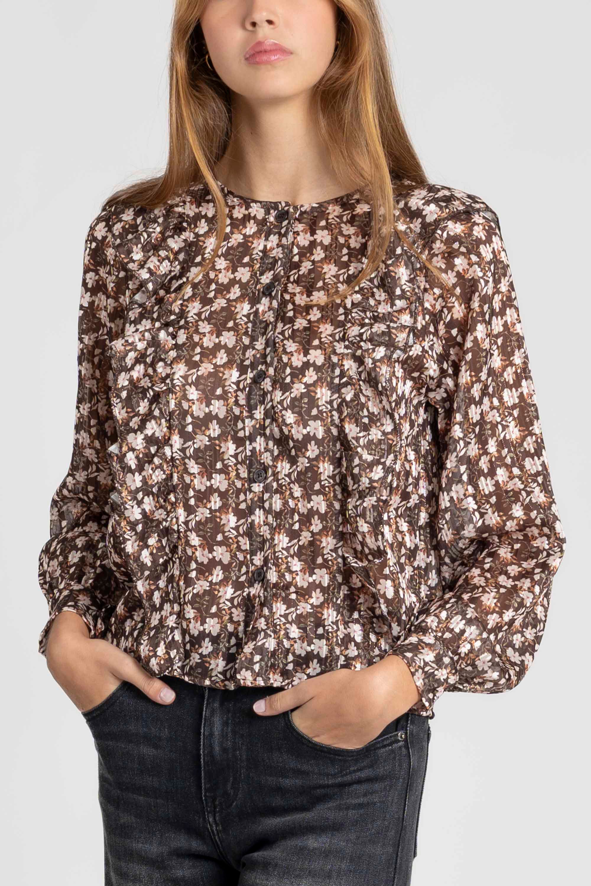 Femme portant une blouse fluide imprimé floral brillante avec des manches longues à volants, affichant un style élégant.
