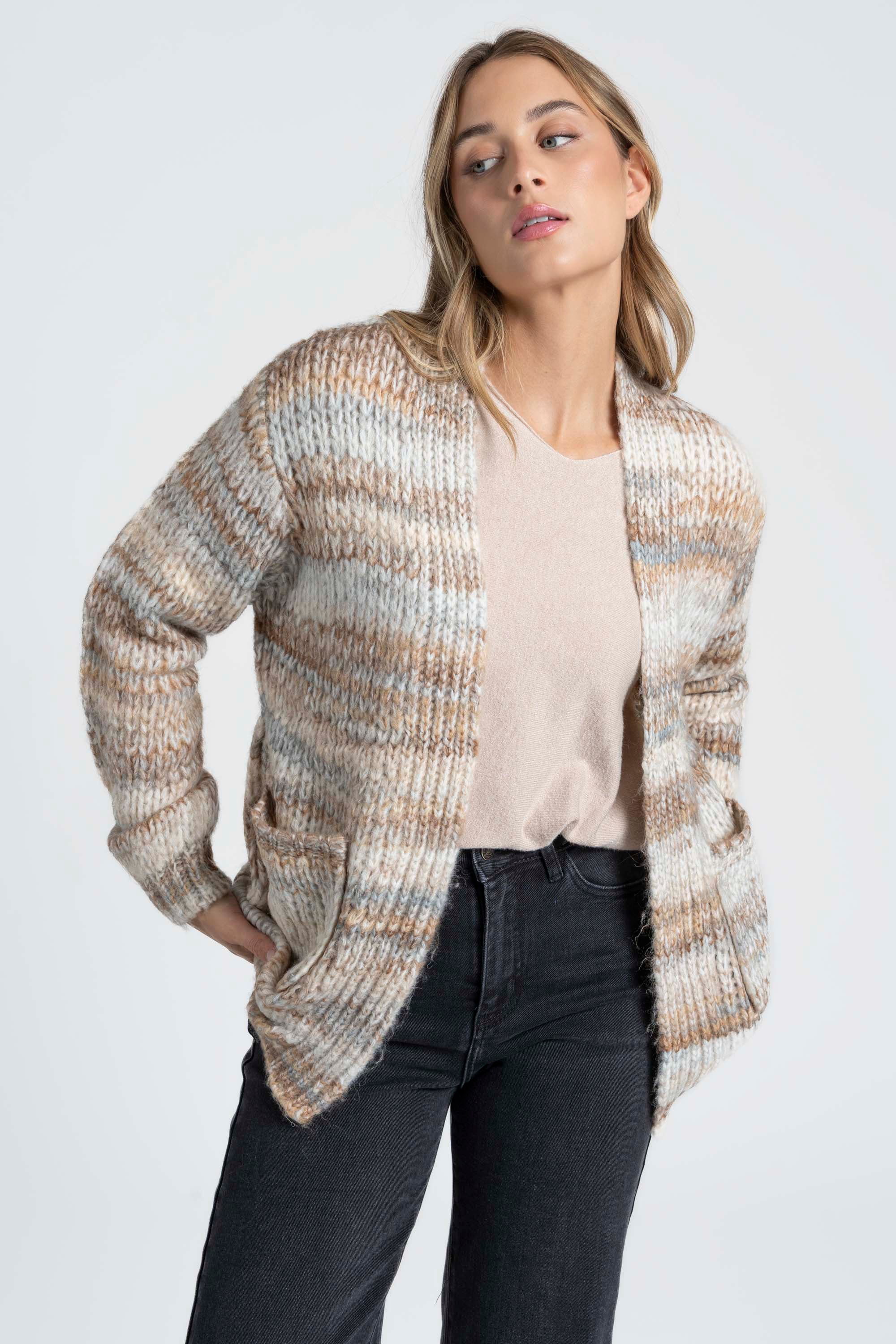 Femme posant avec un cardigan court en maille aux teintes beiges, mettant en valeur le confort et la praticité des poches. C'est un cardigan court femme en maille pour un style chic.