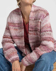 Gros plan sur une femme et son cardigan court en maille, montrant le motif rose et beige. Le cardigan court femme en maille dispose de poches pratiques.