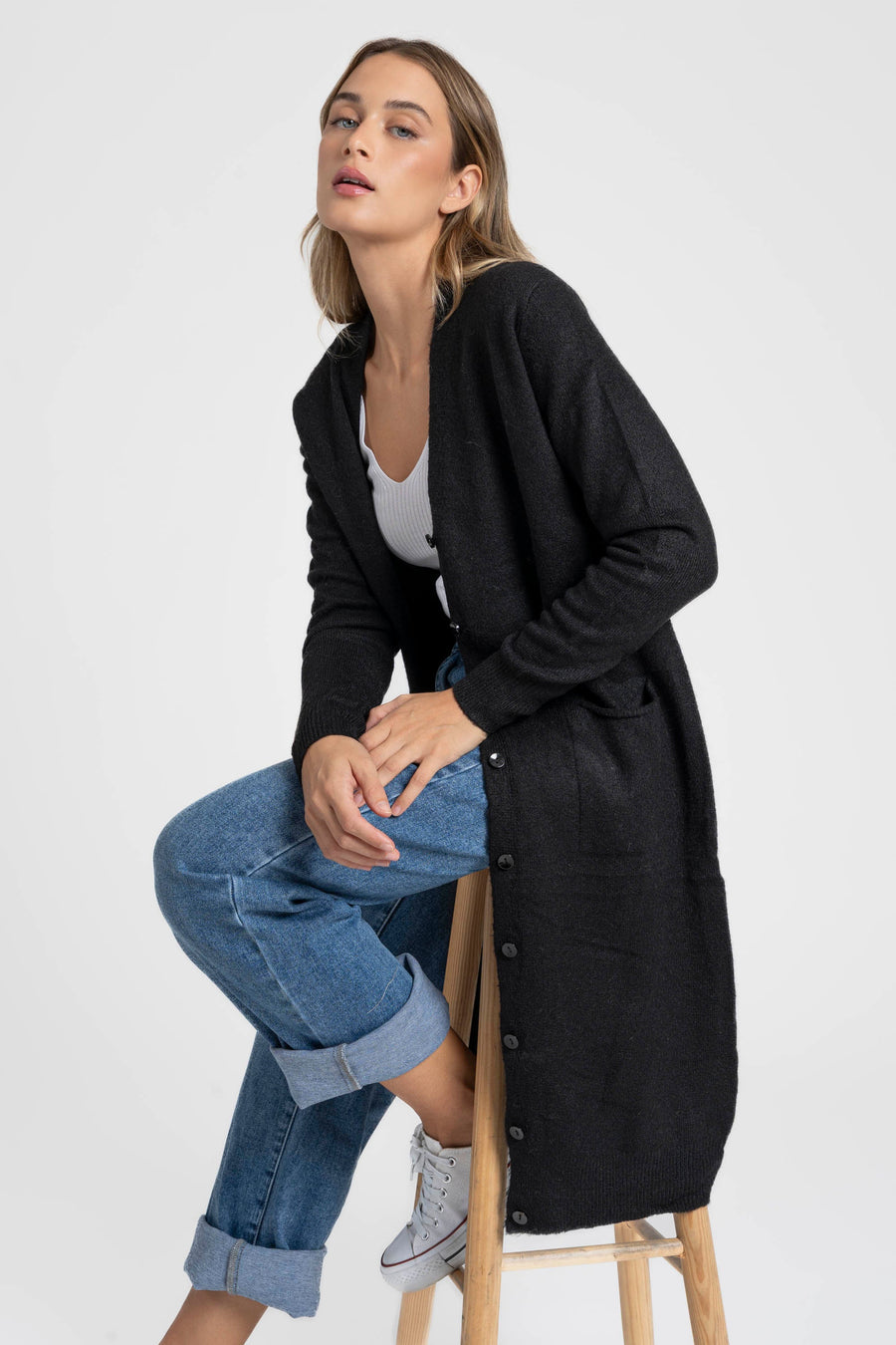 Modèle assise portant un cardigan long femme noir, en laine mélangée, avec des boutons et une structure fluide, parfait pour toute occasion.