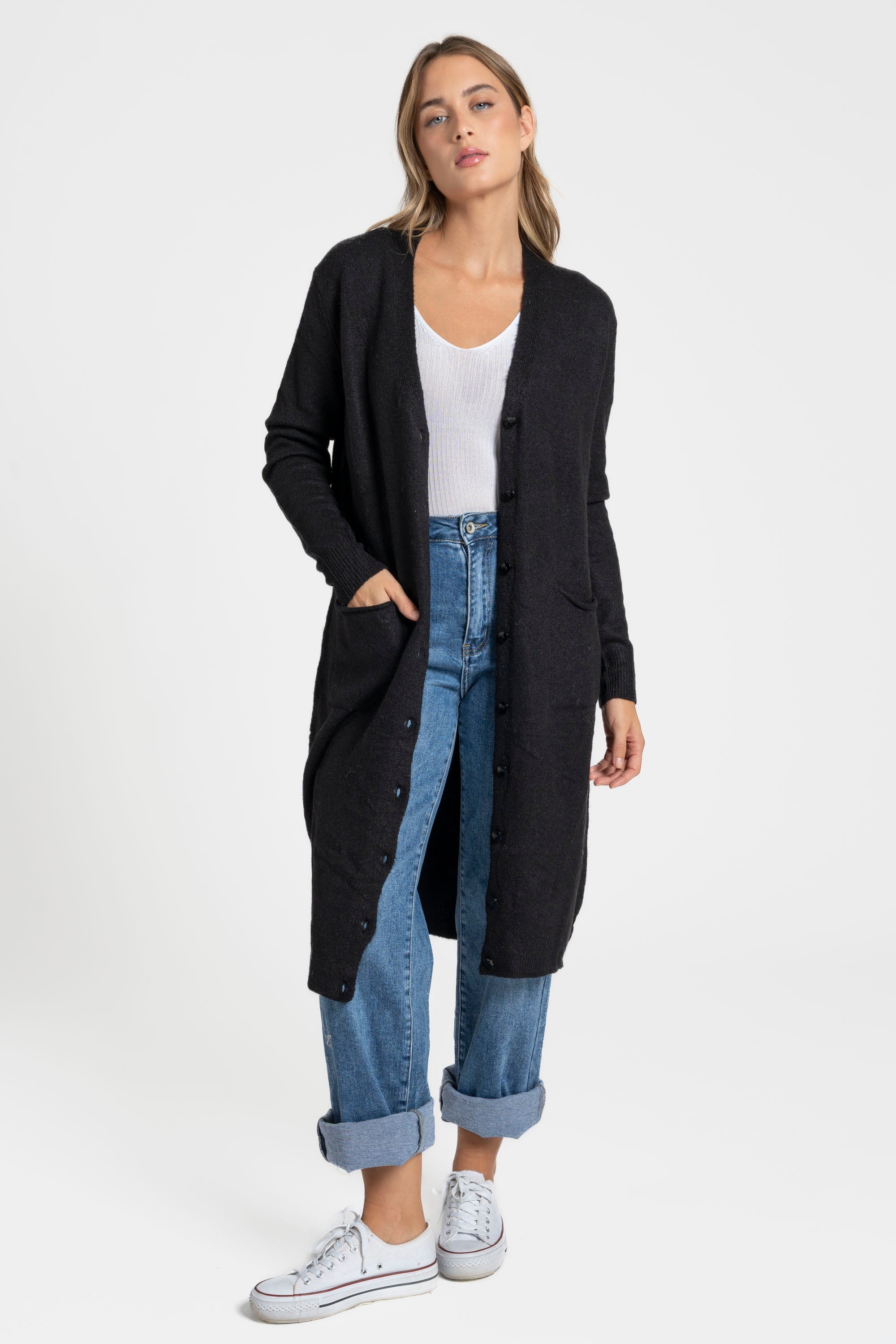 Femme debout avec un cardigan long femme noir, en laine mélangée, avec poches frontales, offrant une allure élégante et décontractée.