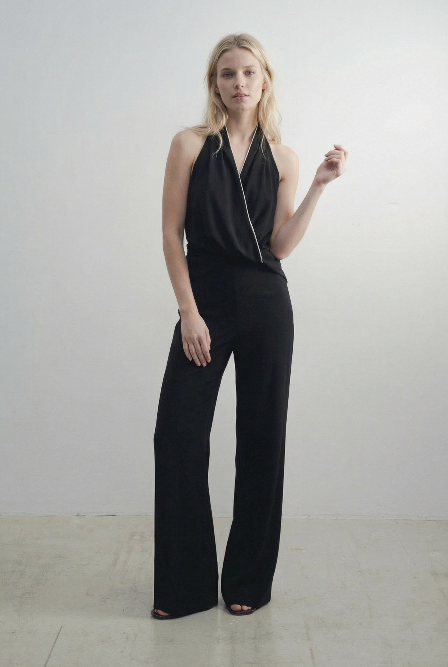 Vue de face d'une combinaison halter noire à nœud, dos nu et jambe large, idéale pour une soirée, représentant la combinaison noire élégante femme.