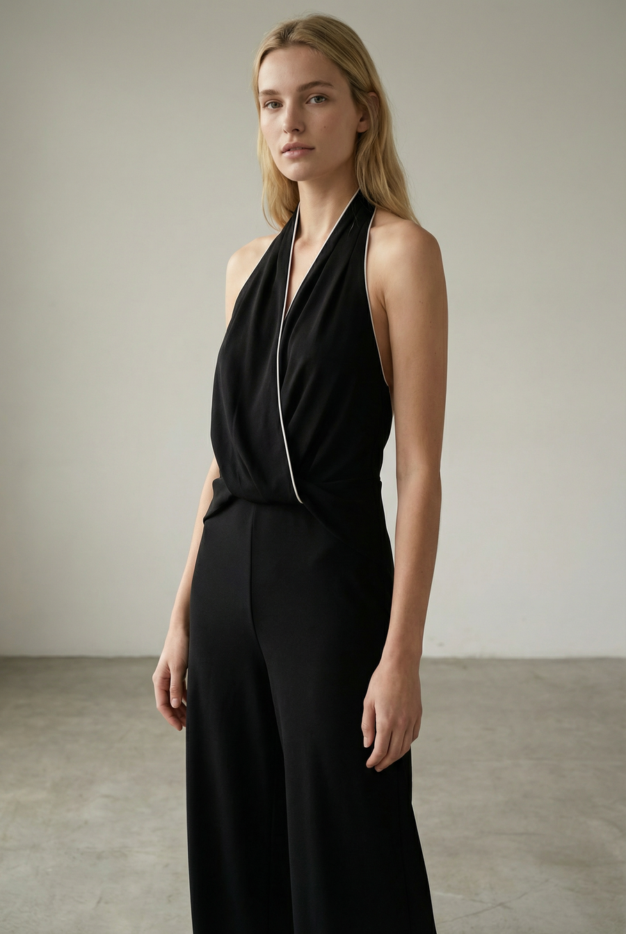 Femme en profil, affichant la combinaison halter noire à nœud, dos nu et jambe large, parfaite pour des événements habillés et stylée en combinaison noire élégante femme.