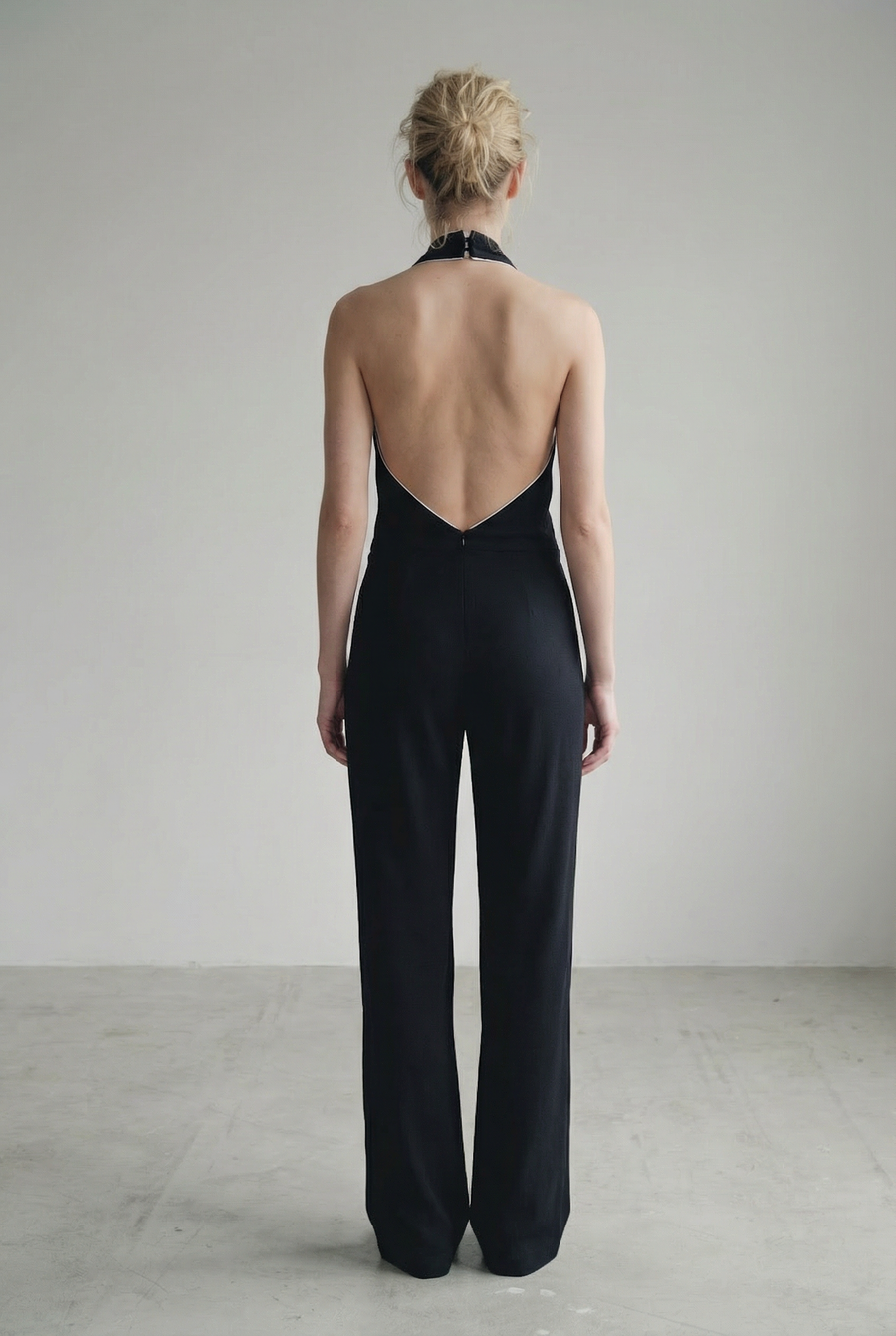 Vue arrière d'une femme portant une combinaison halter noire à nœud, dos nu et jambe large, illustrant l'allure et le style de la combinaison noire élégante femme.