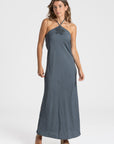 Femme dans une robe midi halter fluide en viscose bleu-gris, avec un détail floral, idéale pour une tenue estivale.
