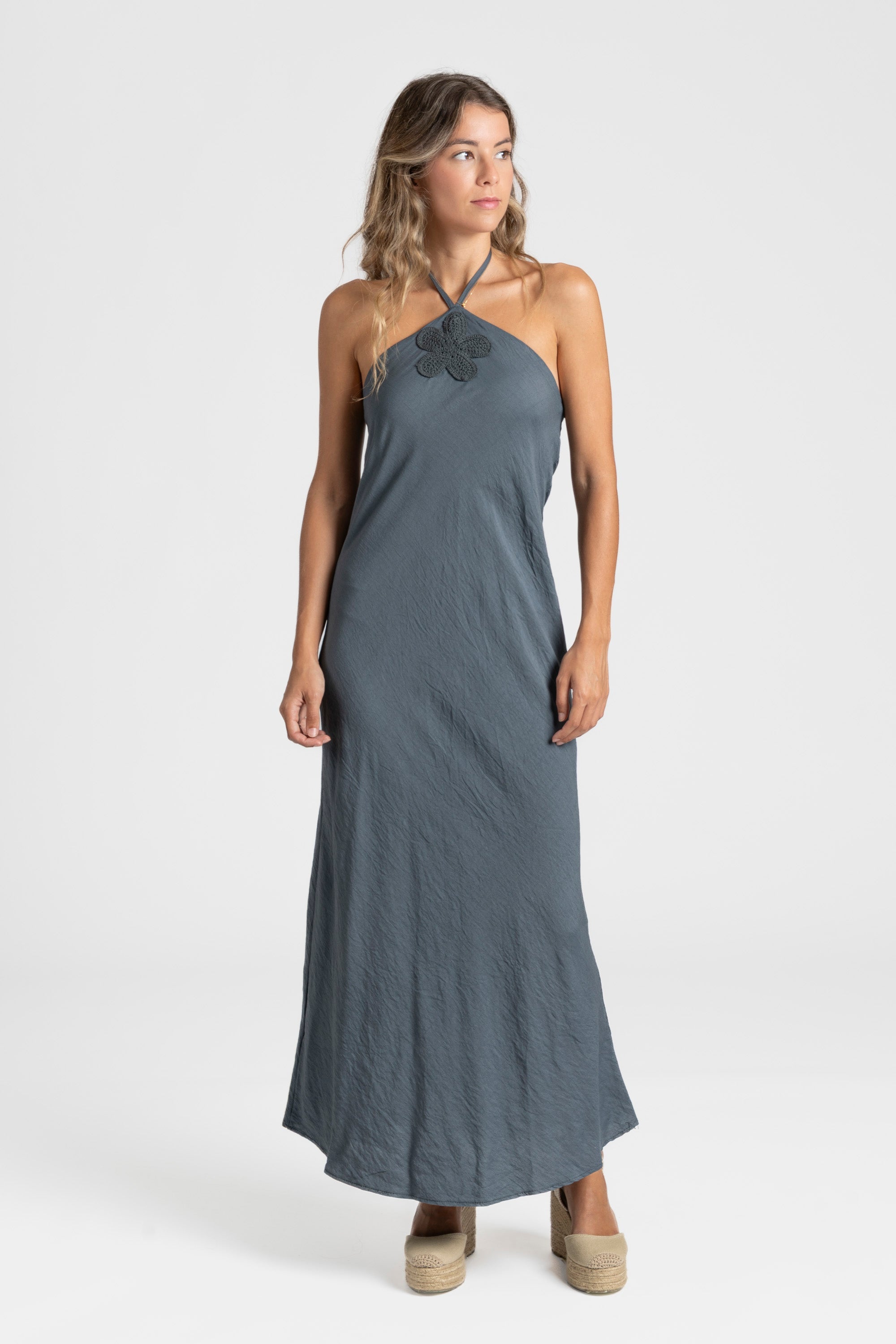 Modèle portant une robe midi halter fluide en viscose bleu-gris, avec des accessoires délicats, pour un look estival.