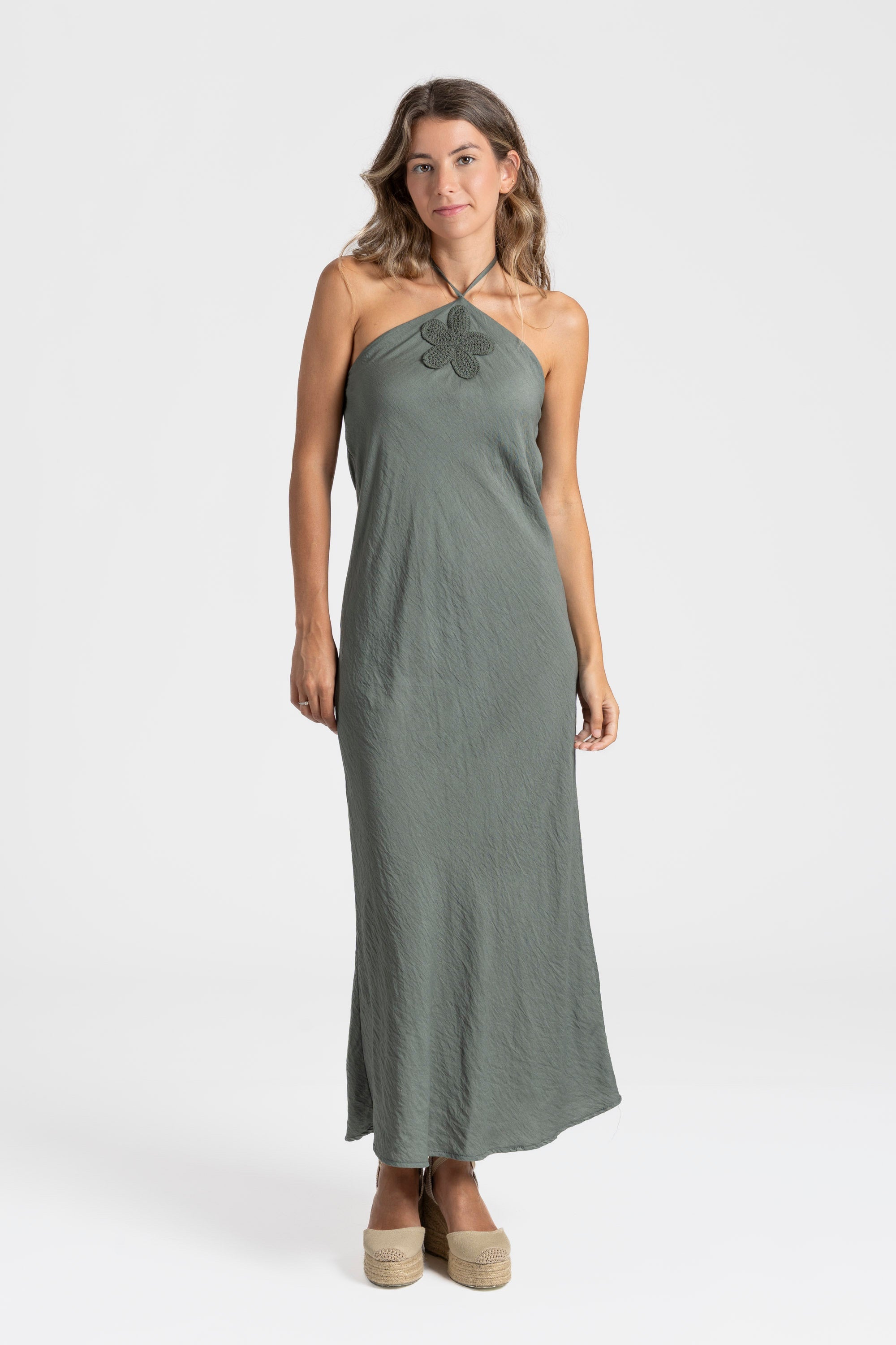 Femme dans une robe midi halter fluide en viscose verte, parfaite pour l'été, avec des sandales pour un look décontracté.