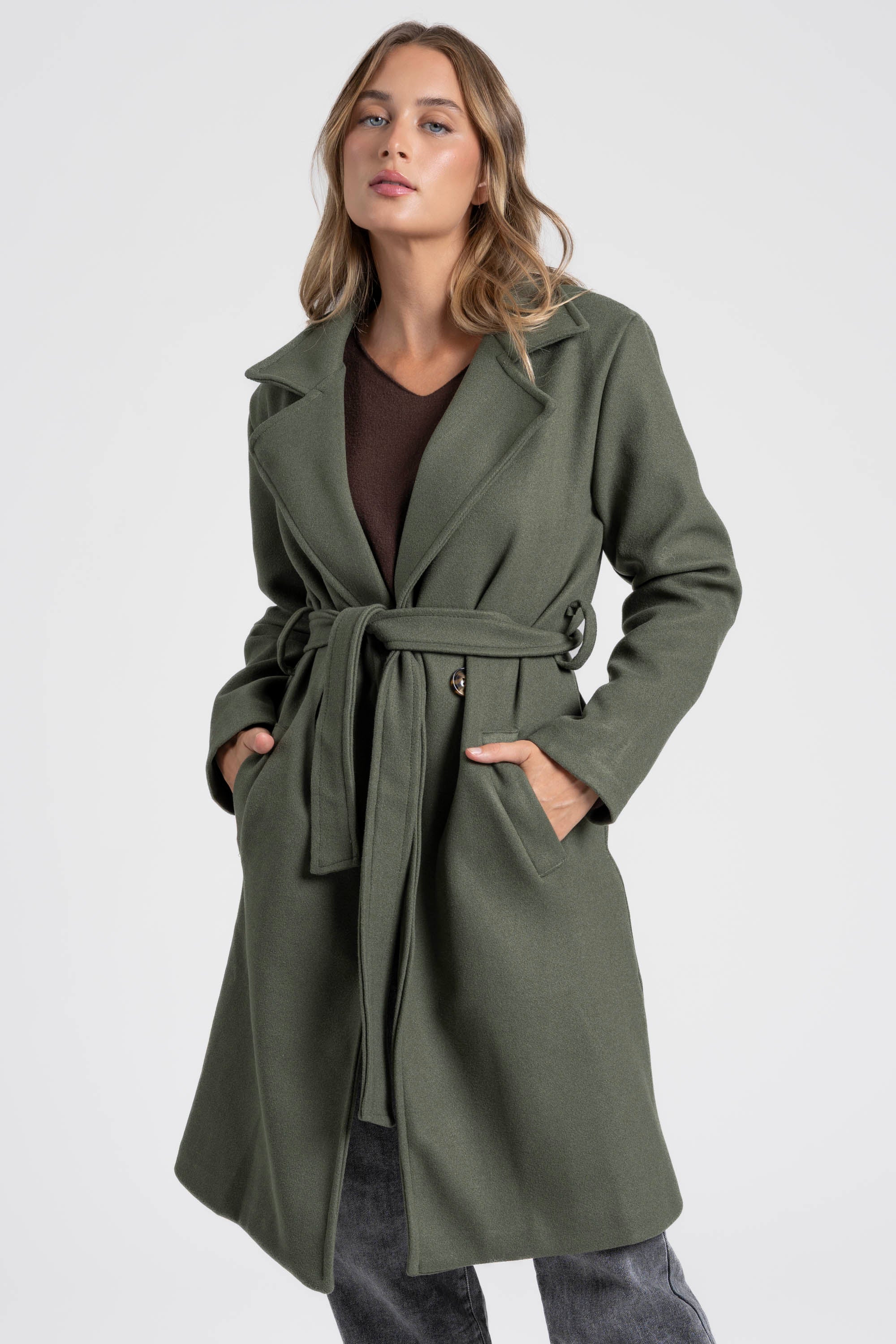 Vue en légère perspective du manteau croisé femme vert, mettant en avant la ceinture et les poches.