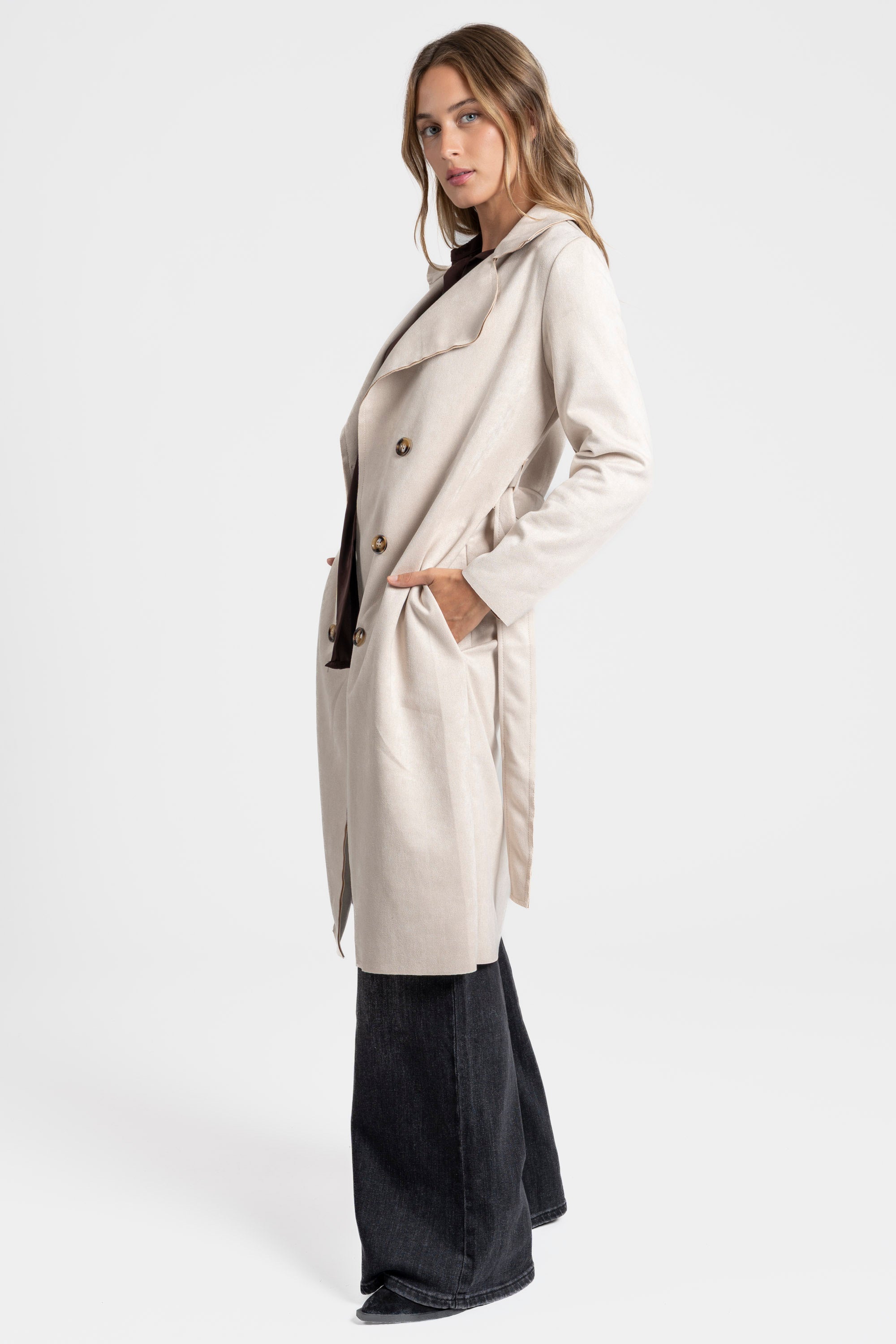 Trench femme ceinture beige en profile, soulignant sa coupe fluide et ses manches longues.