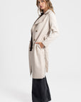Trench femme ceinture beige en profile, soulignant sa coupe fluide et ses manches longues.