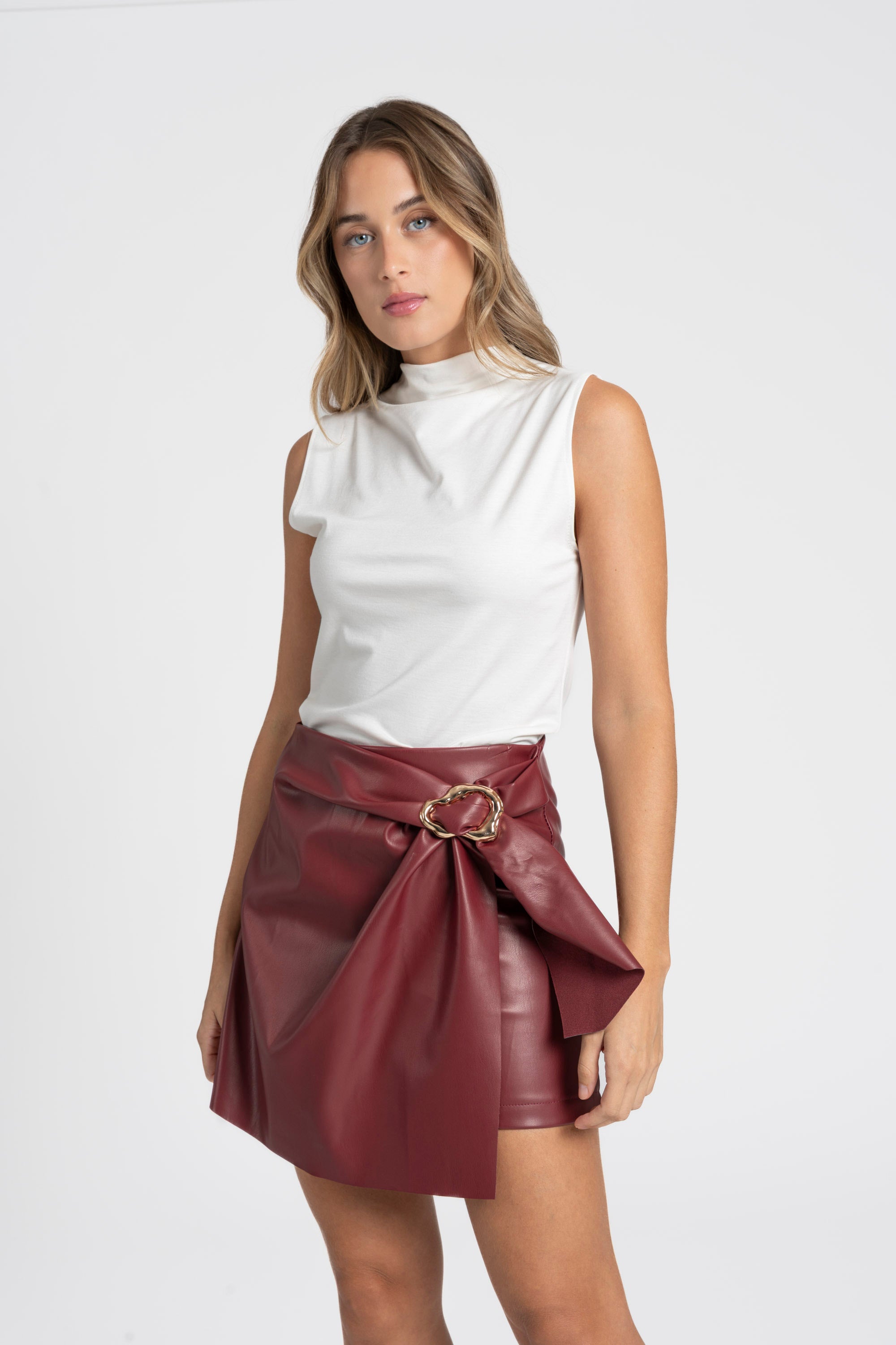 Femme portant une jupe similicuir taille haute bordeaux avec un haut blanc, affichant un look élégant.
