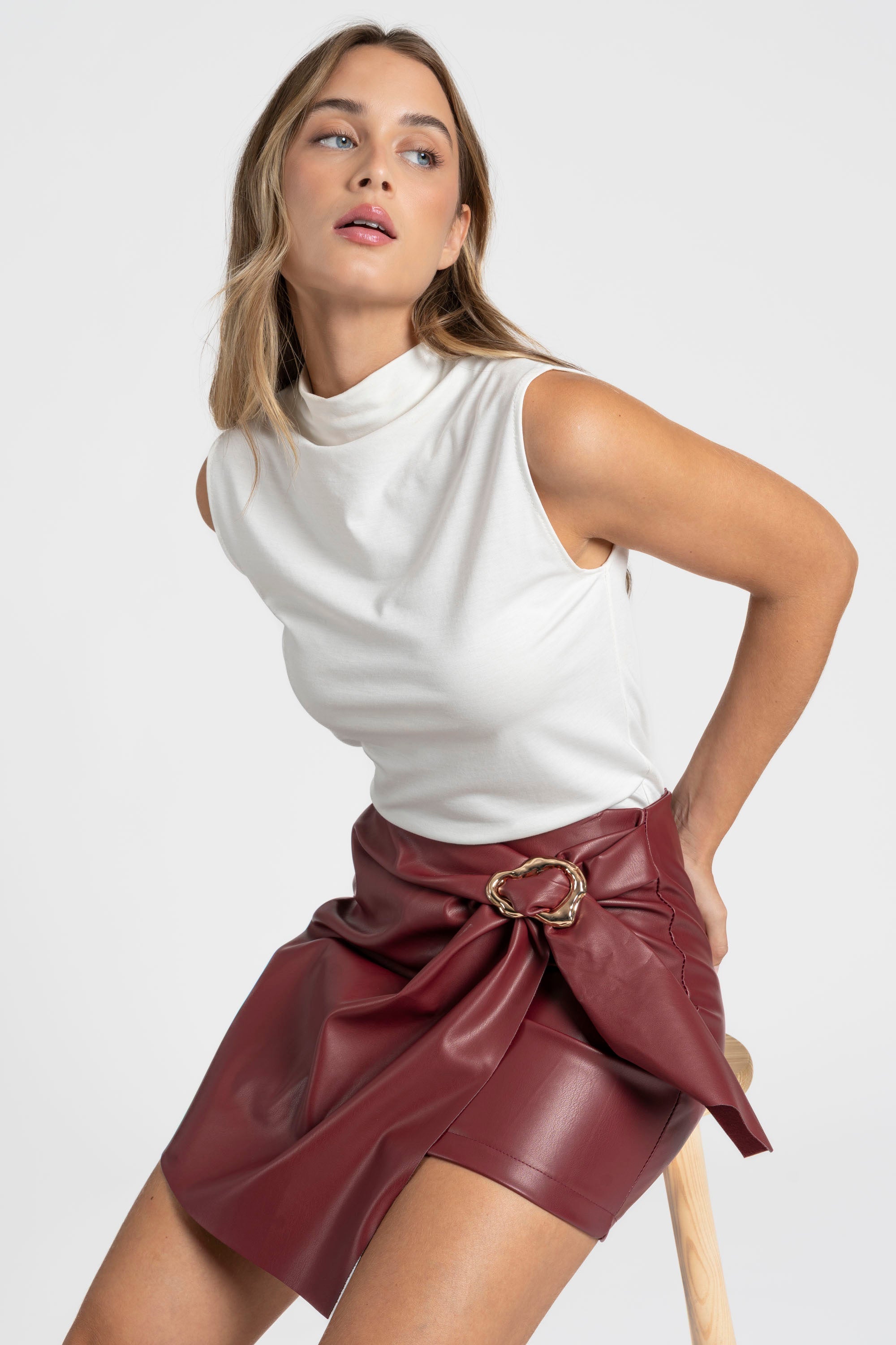 Femme utilisant une jupe similicuir taille haute rouge dans une pose naturelle, style partagé sur le devant.