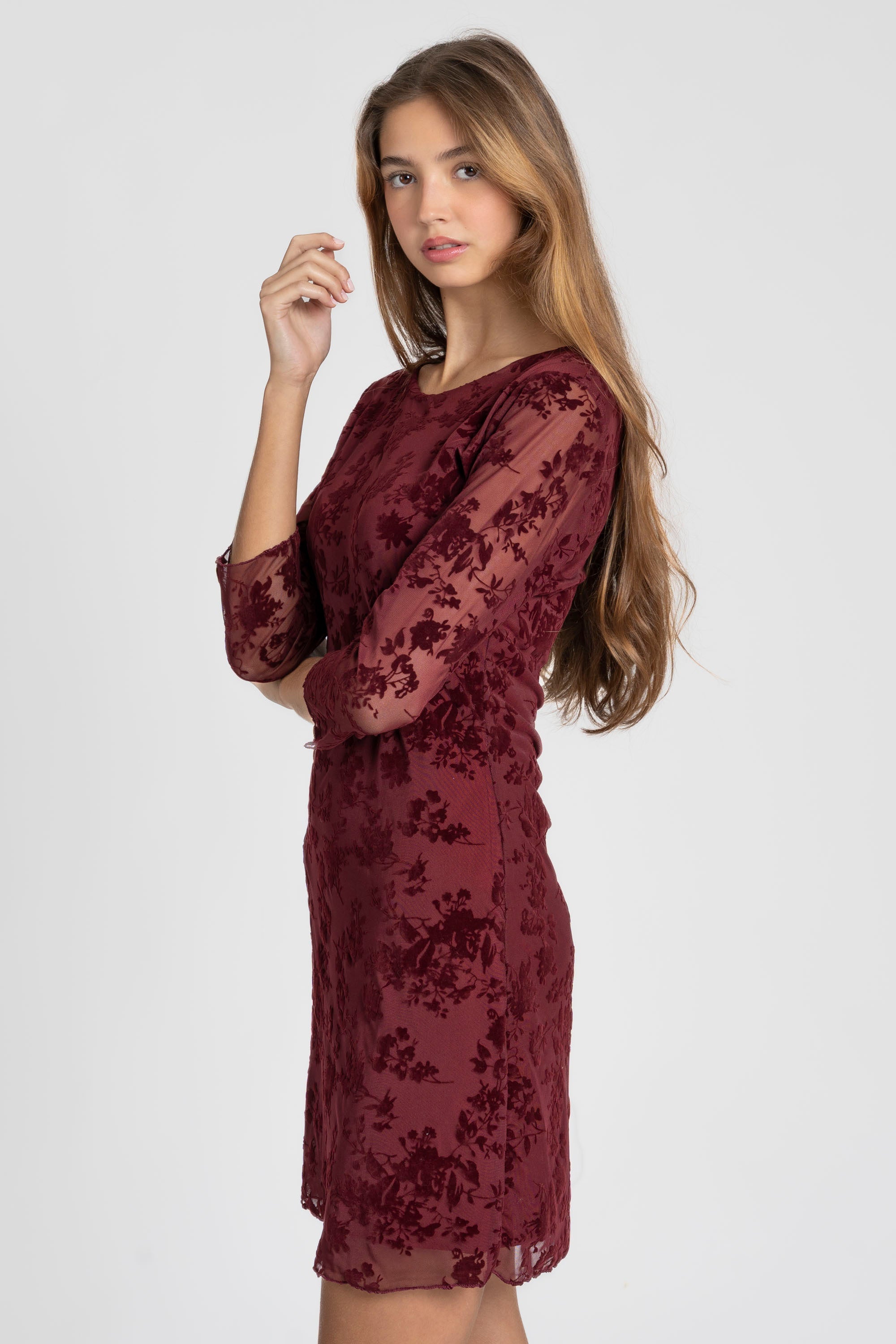 Vue de profil d'une femme portant une robe courte dentelle chic manches 3/4 bordeaux, soulignant la coupe élégante. Parfaite pour des soirées chic, robe courte dentelle.