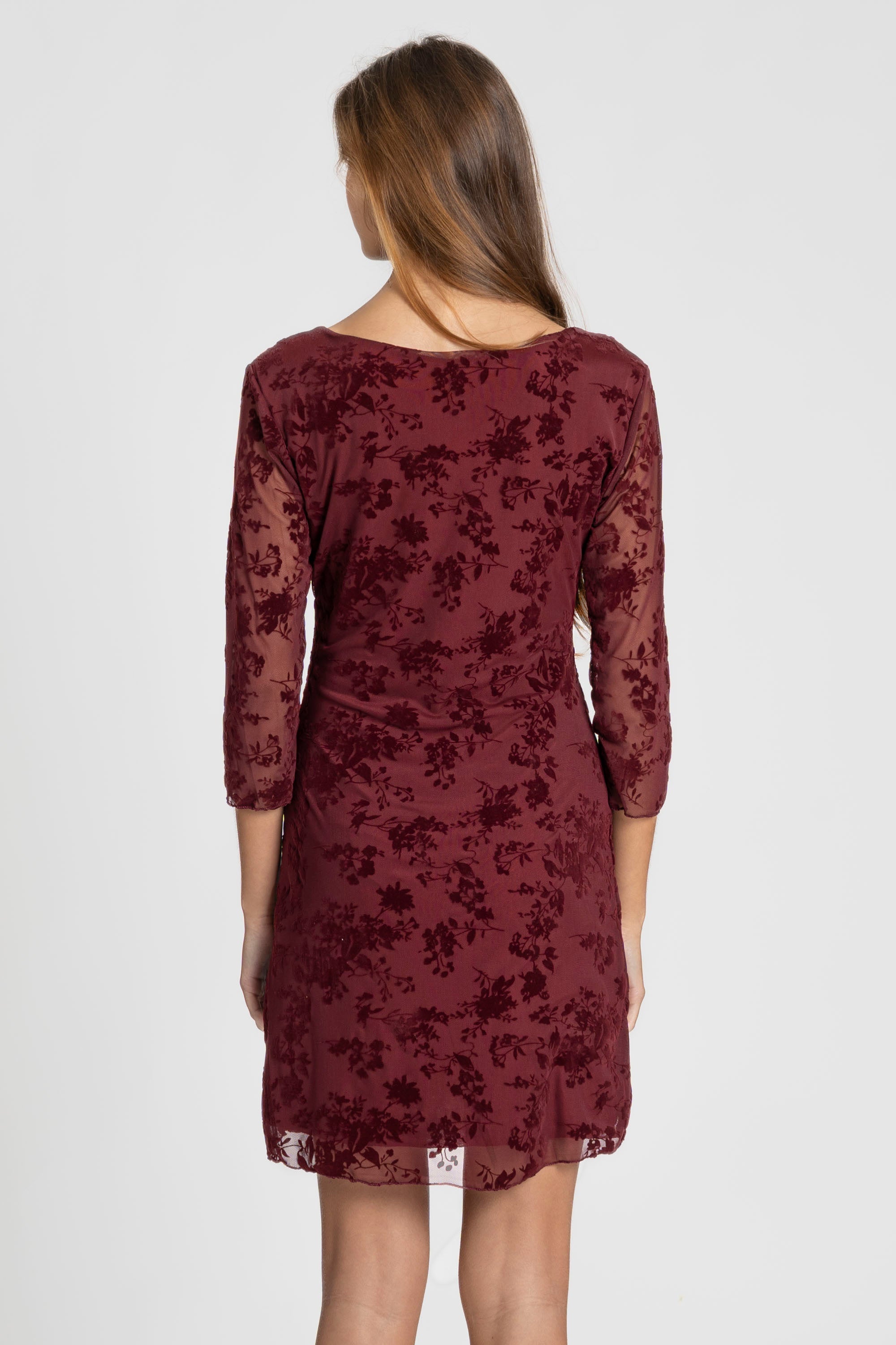 Femme de dos enrobe courte dentelle chic manches 3/4 bordeaux, dévoilant la délicatesse de la dentelle. Un choix élégant pour un look de soirée, robe courte dentelle.