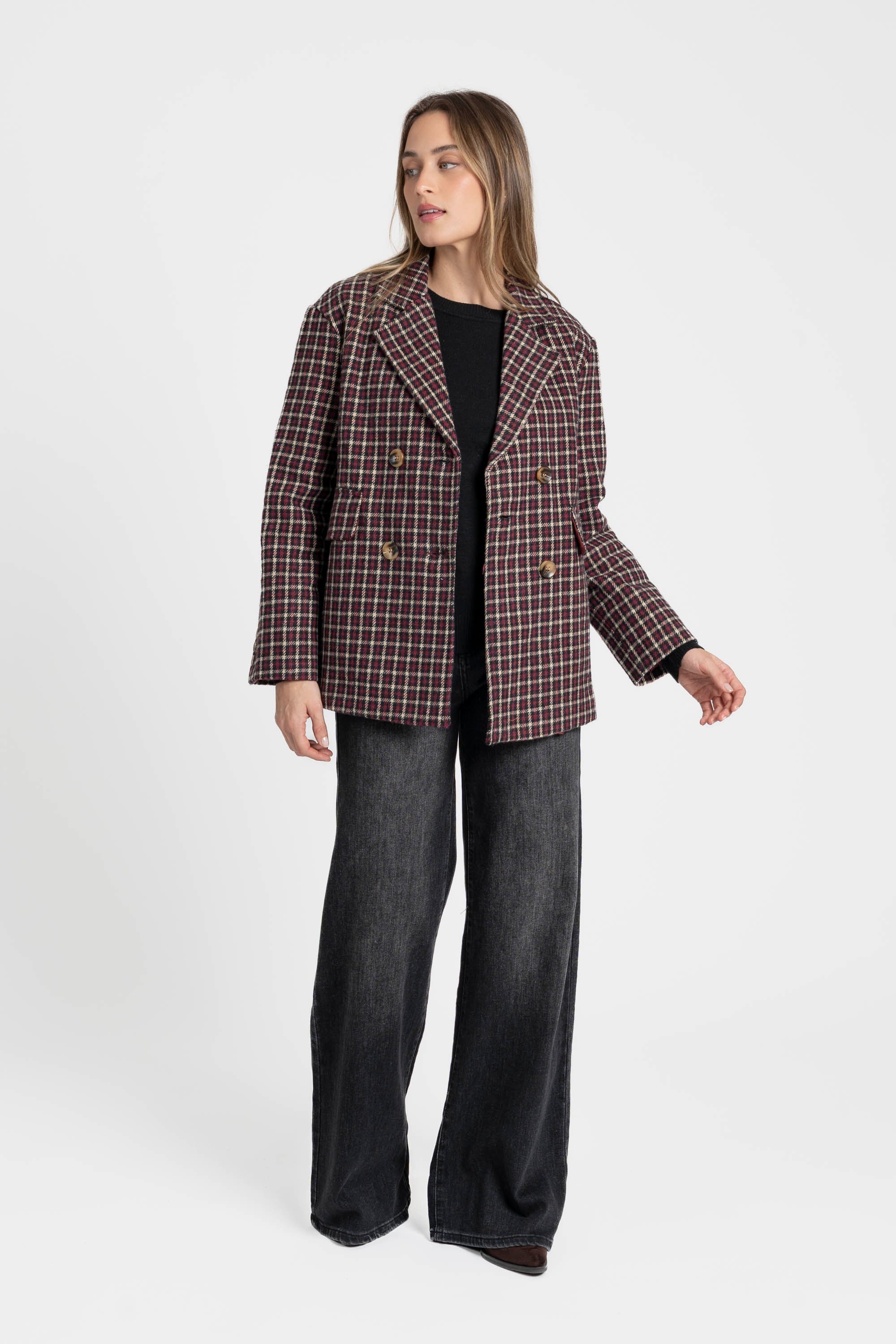 Femme portant un blazer coton bordeaux et marron, coupe élégante, avec un motif de carreaux en se tenant debout, pantalon large