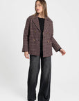 Femme portant un blazer coton bordeaux et marron, coupe élégante, avec un motif de carreaux en se tenant debout, pantalon large