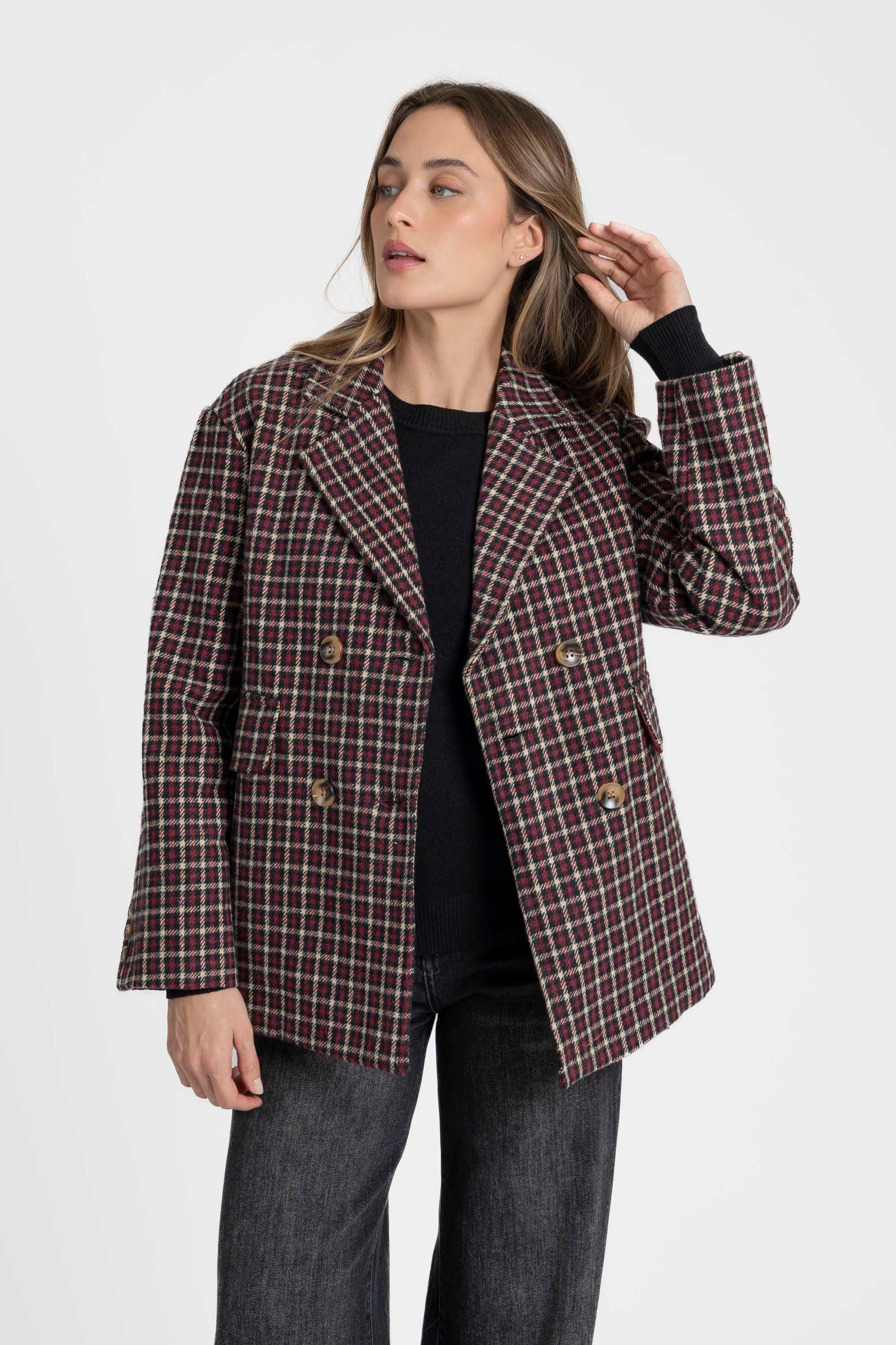 Gros plan sur une femme avec un blazer coton femme bordeaux et marron, coupe élégante, touchant ses cheveux, mettant en valeur le tissu à carreaux