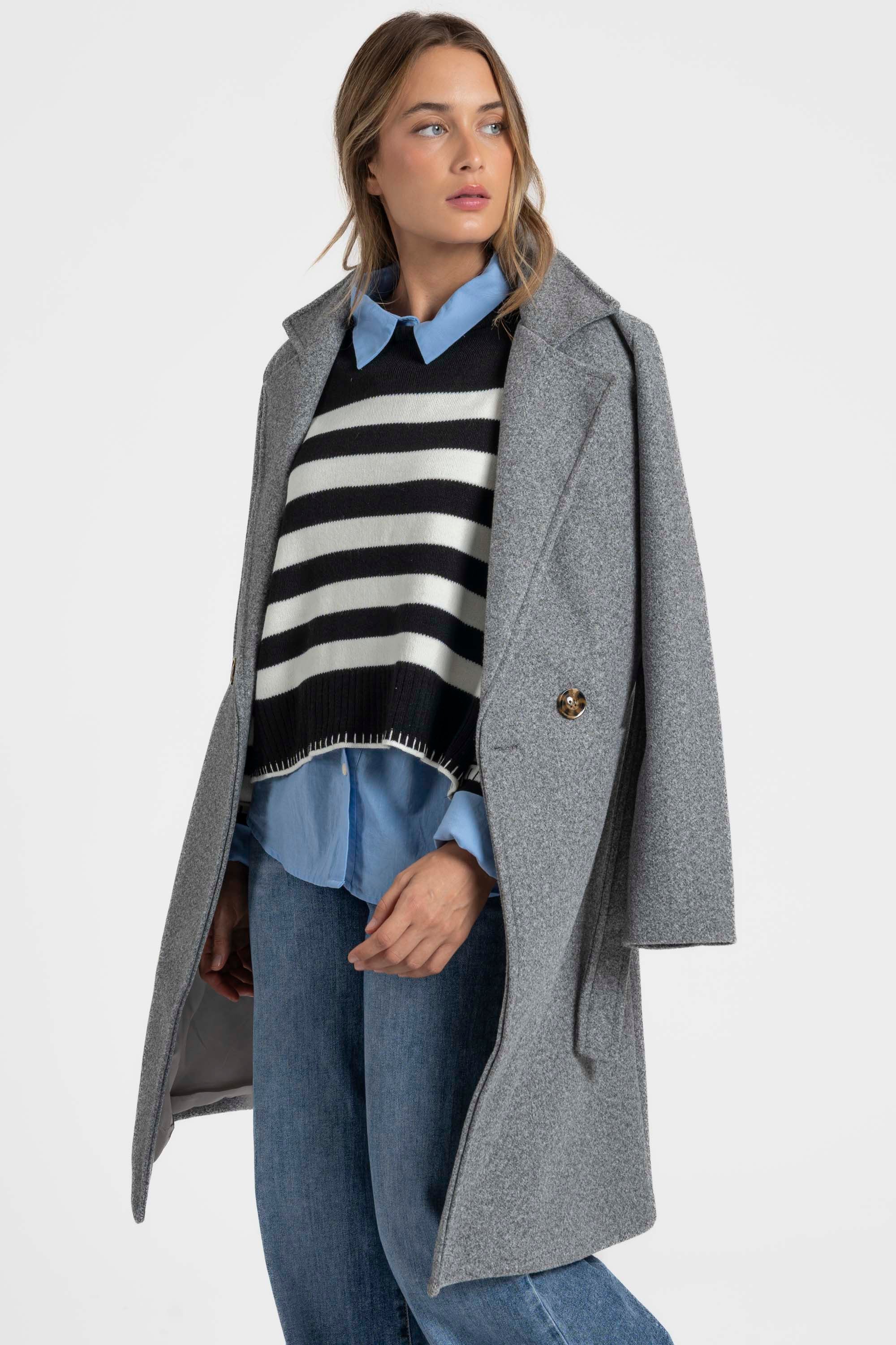 Manteau croisé femme élégant en gris porté avec un pull noir et blanc, parfait pour les looks mi-saison.