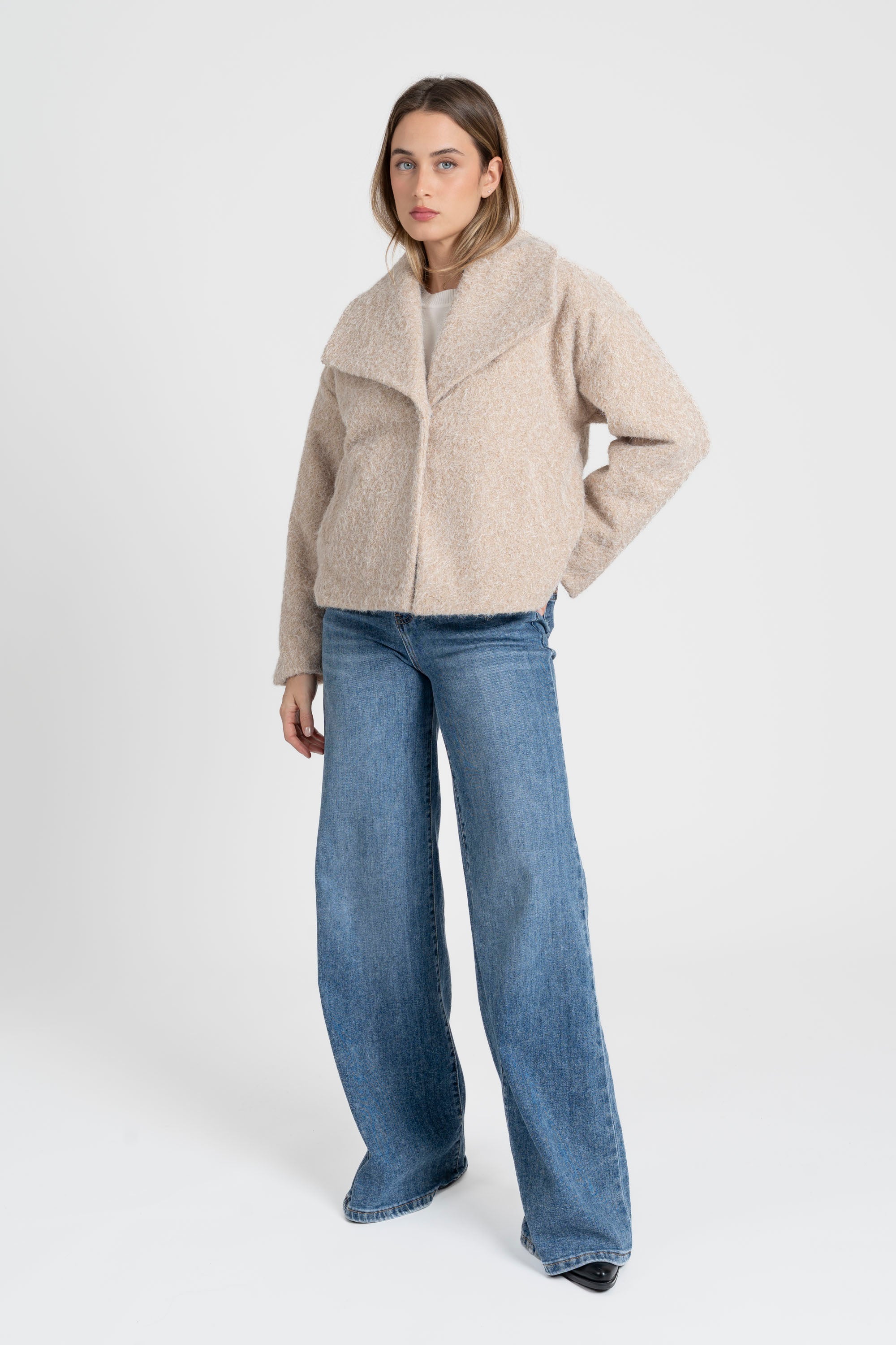 Femme portant une veste courte effet poil doublée col à revers en couleur beige, stylée avec un jean, pour un look contemporaine. Veste courte femme.