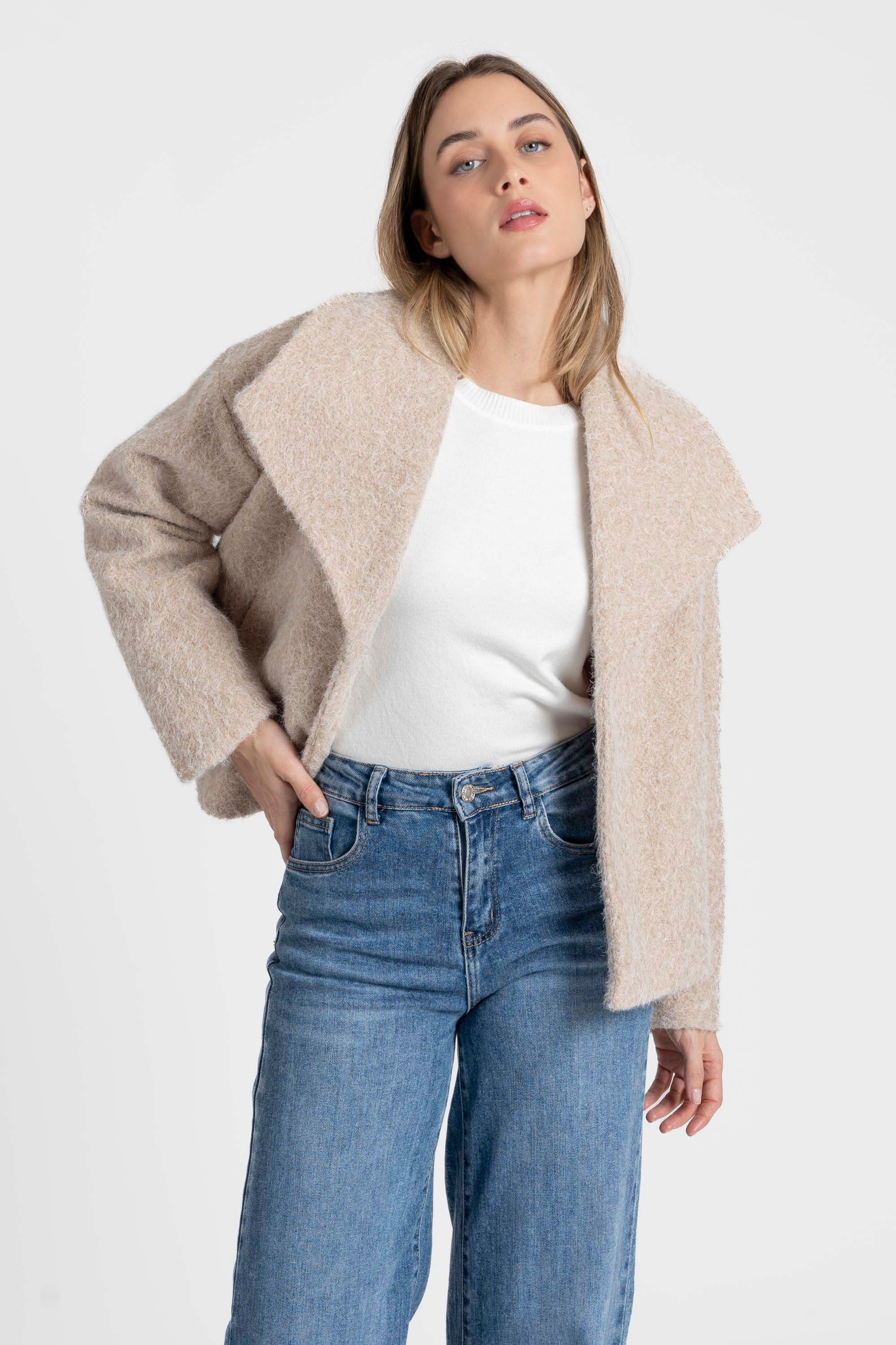 Femme dans une veste courte effet poil doublée col à revers beige, ajoutant une touche de modernité à son look avec un jean. Veste courte femme.