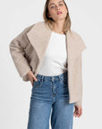 Femme dans une veste courte effet poil doublée col à revers beige, ajoutant une touche de modernité à son look avec un jean. Veste courte femme.