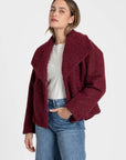 Femme avec une veste courte effet poil doublée col à revers en rouge, associée à un jean, parfaite pour un look d'automne. Veste courte femme.