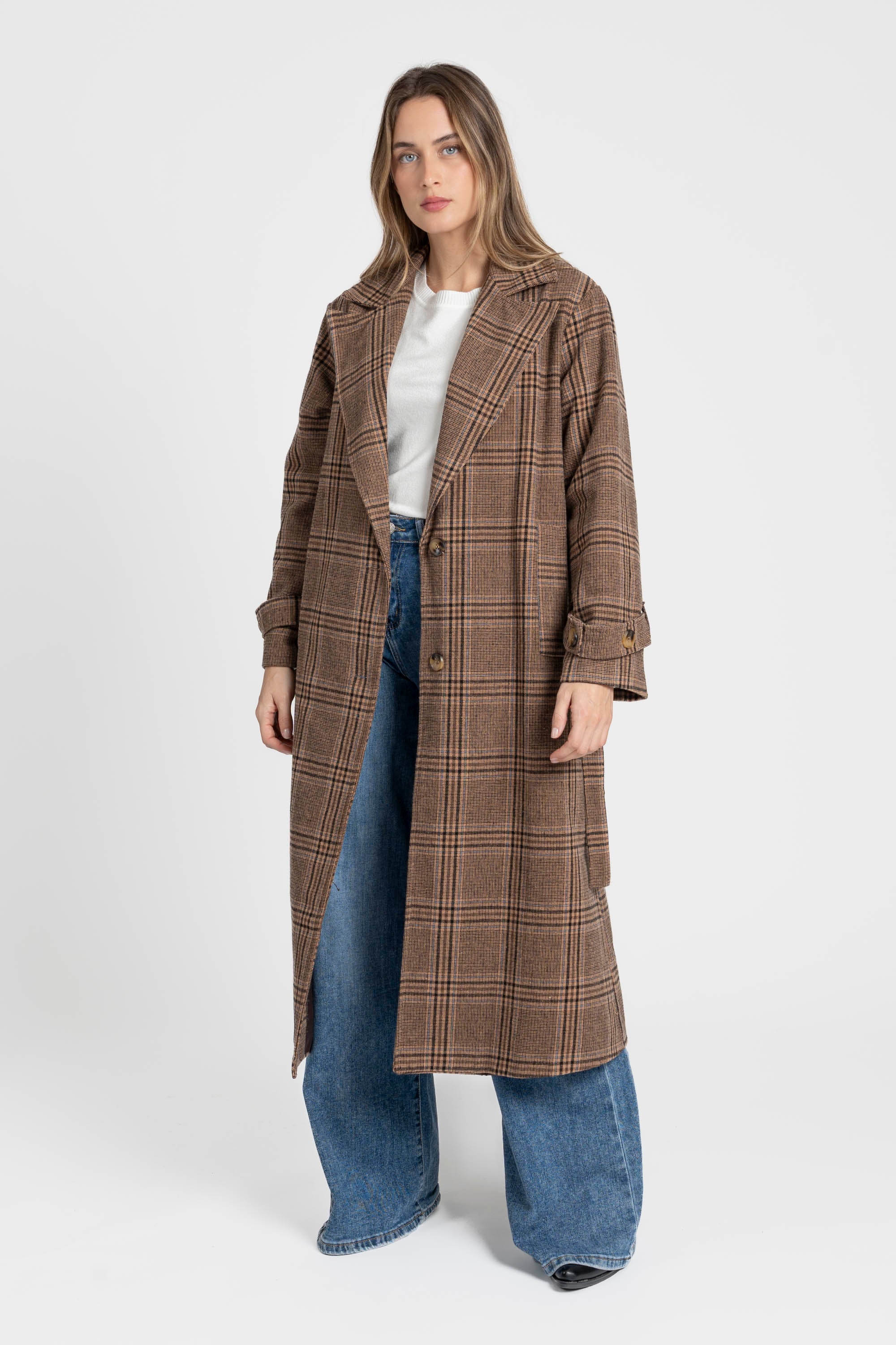Manteau long femme en coton coupe ceinturée, porté par une femme devant un fond blanc, affichant un motif à carreaux marron avec pantalon large.