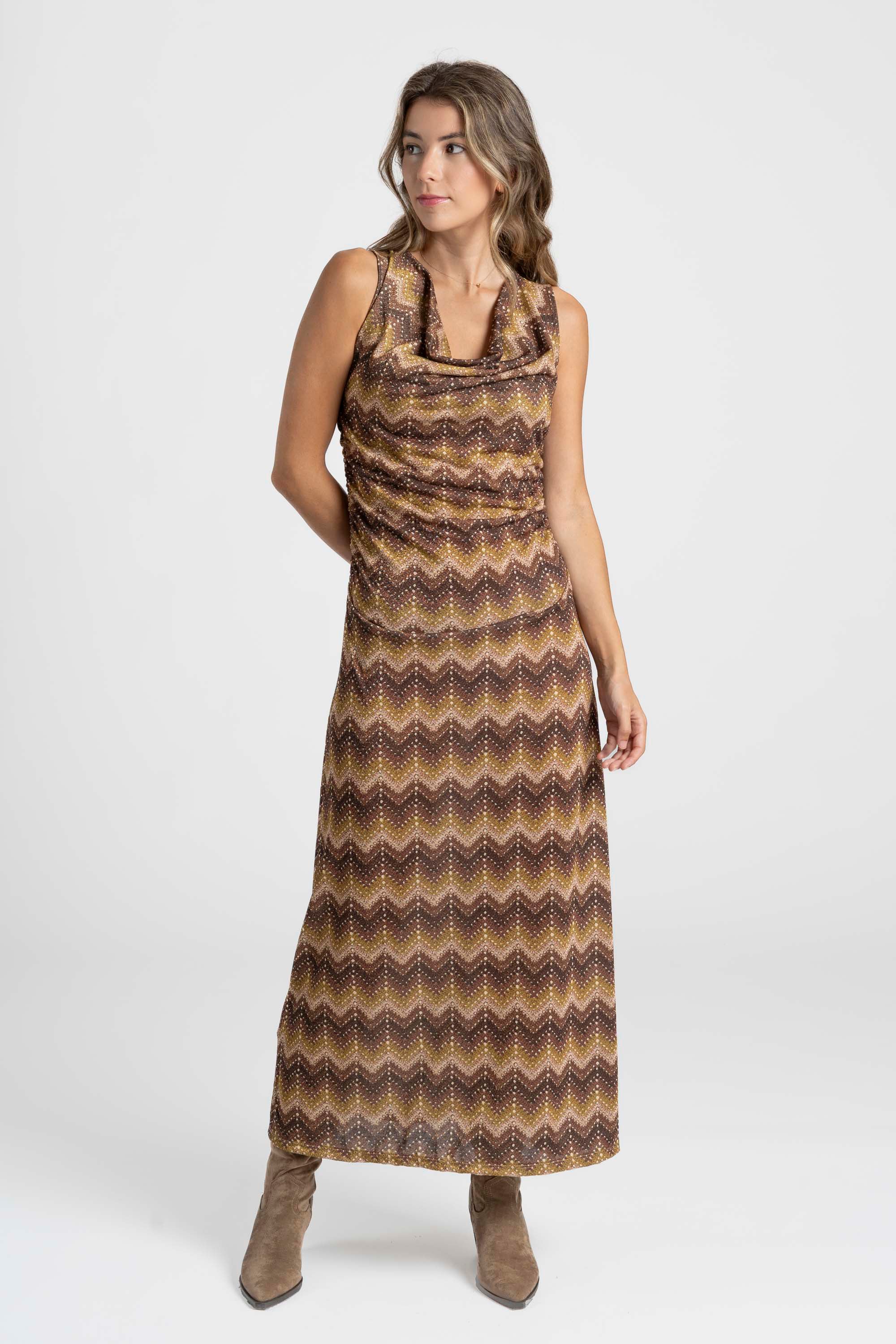 Modèle à la pose élégante portant une robe longue fluide avec motifs marron, polyvalente pour les sorties et les événements.