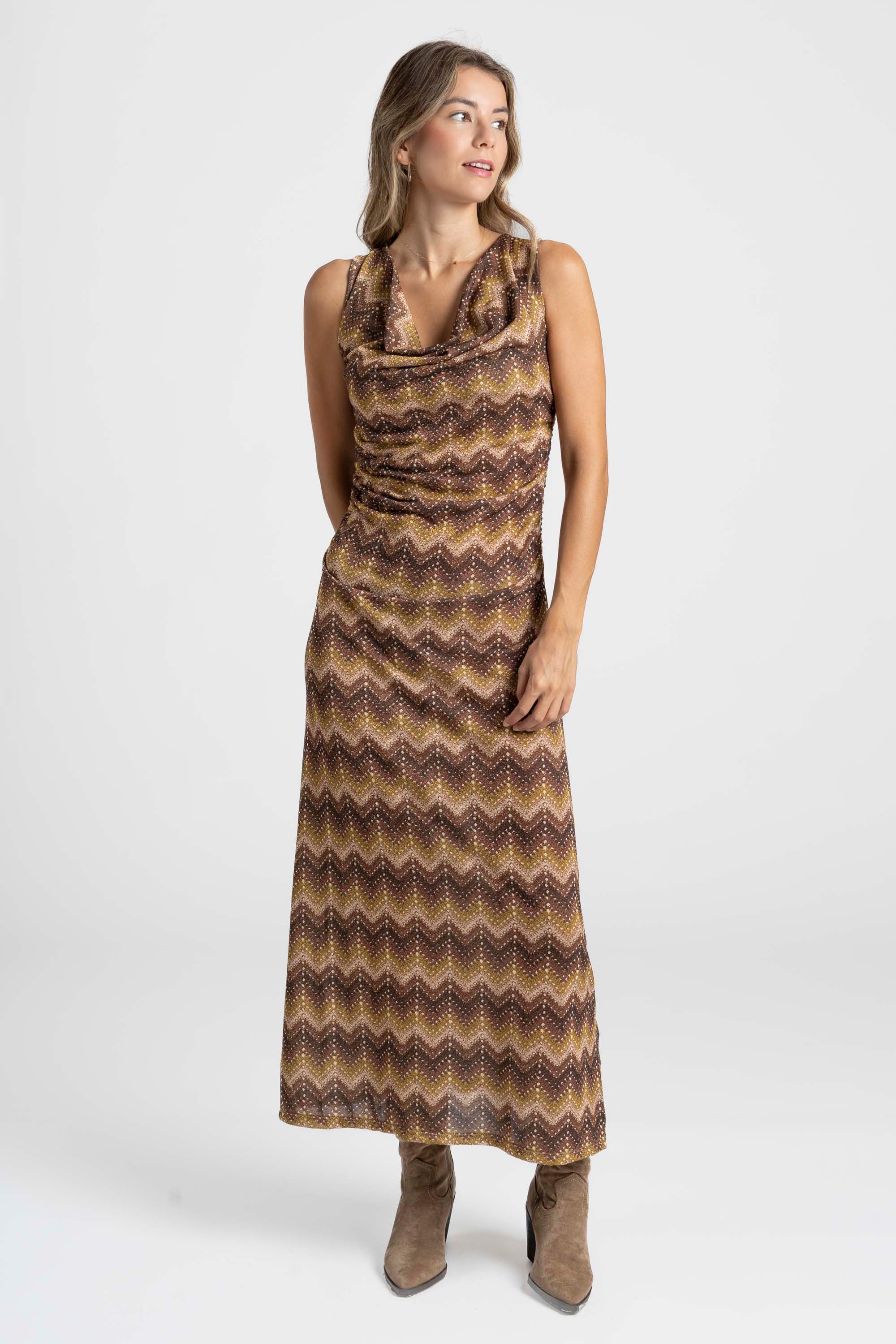 Modèle portant une robe longue fluide à motifs marron et dorés, coupe sans manches col V, parfaite pour les occasions décontractées.