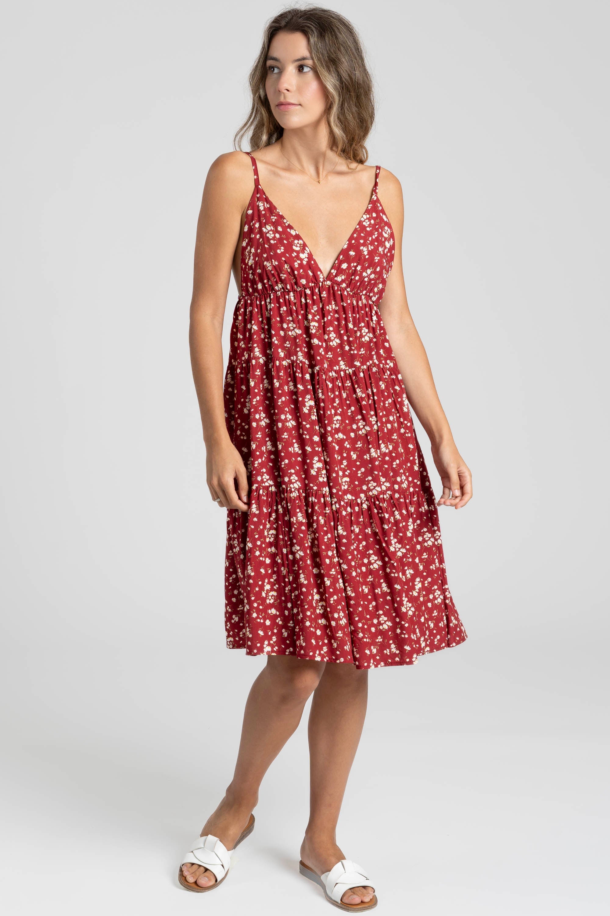 Modele en position debout, robe fluide en viscose à bretelles fines, couleur bordeaux, avec un design évasé.