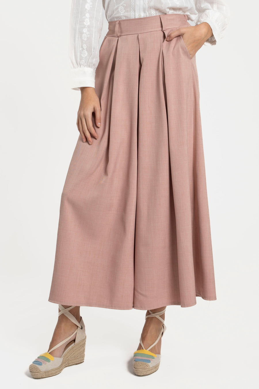Femme en pantalon fluide taille haute femme rose, avec une blouse blanche, posant avec élégance et naturel.