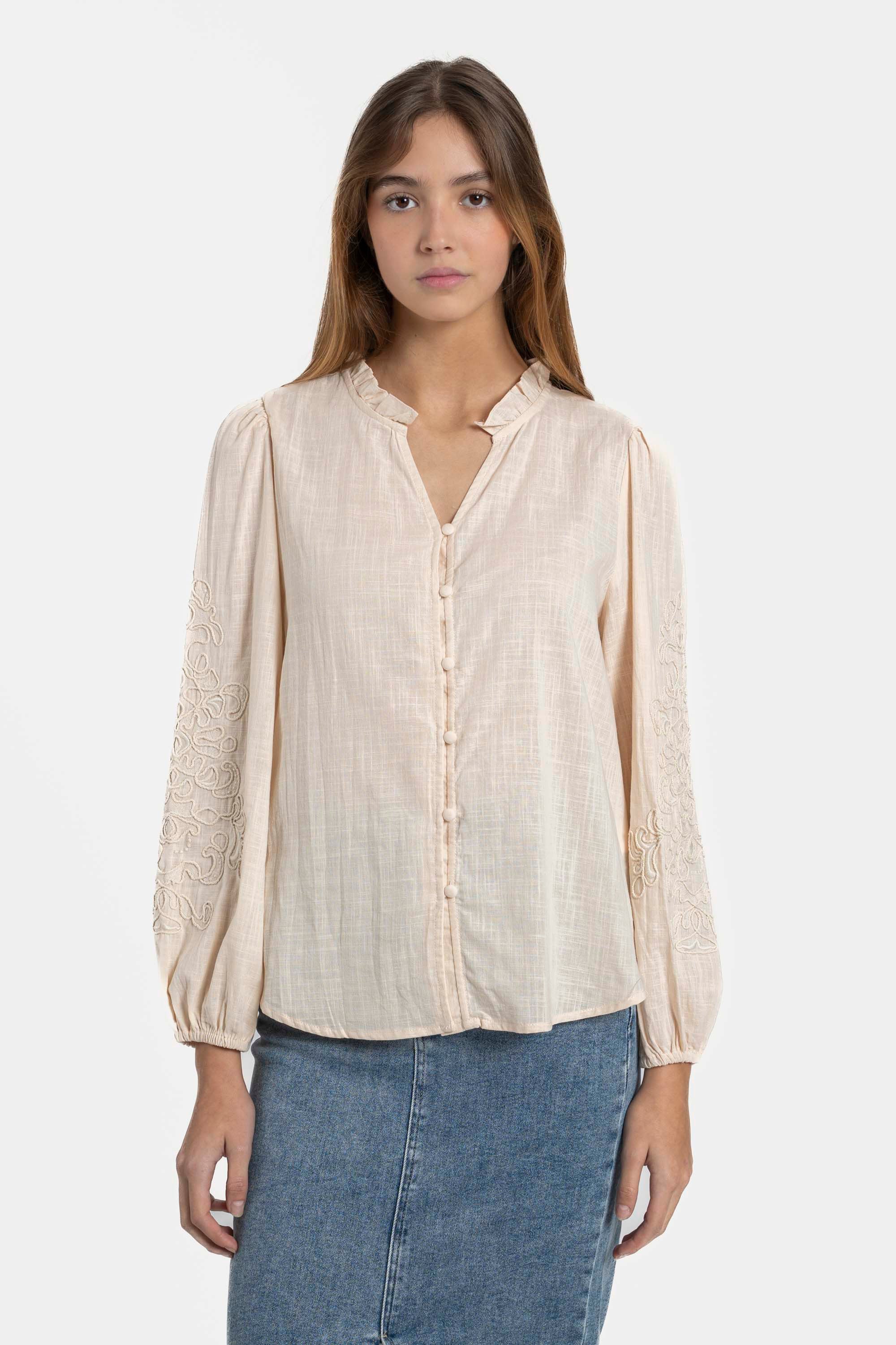 Femme portant une chemise brodée en coton de couleur clair, avec manches longues élégantes, parfaite pour toutes les occasions. Chemise brodée femme tendance.