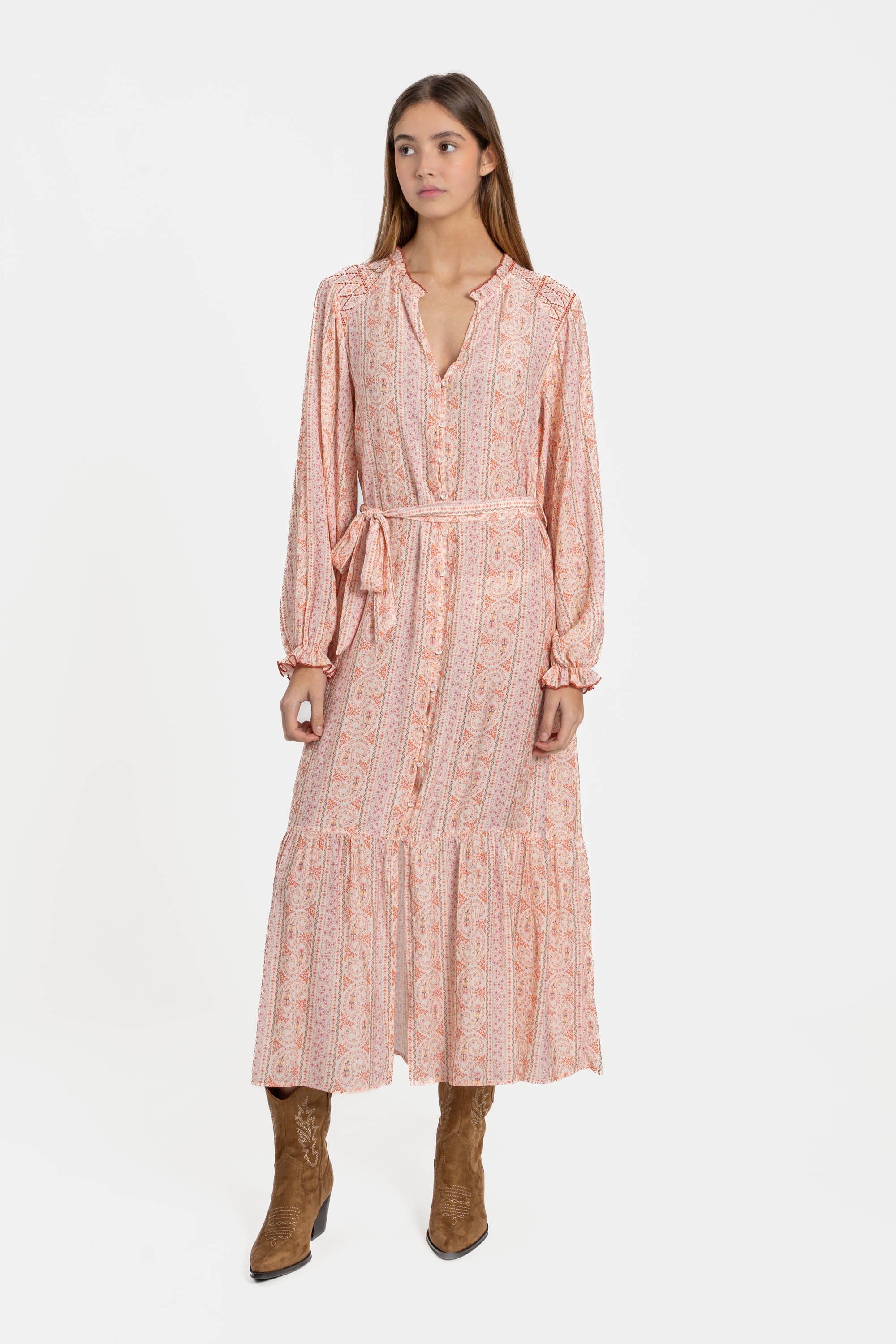 Femme debout en robe longue fluide imprimée avec ceinture rose, illustrant une allure chic et féminine.