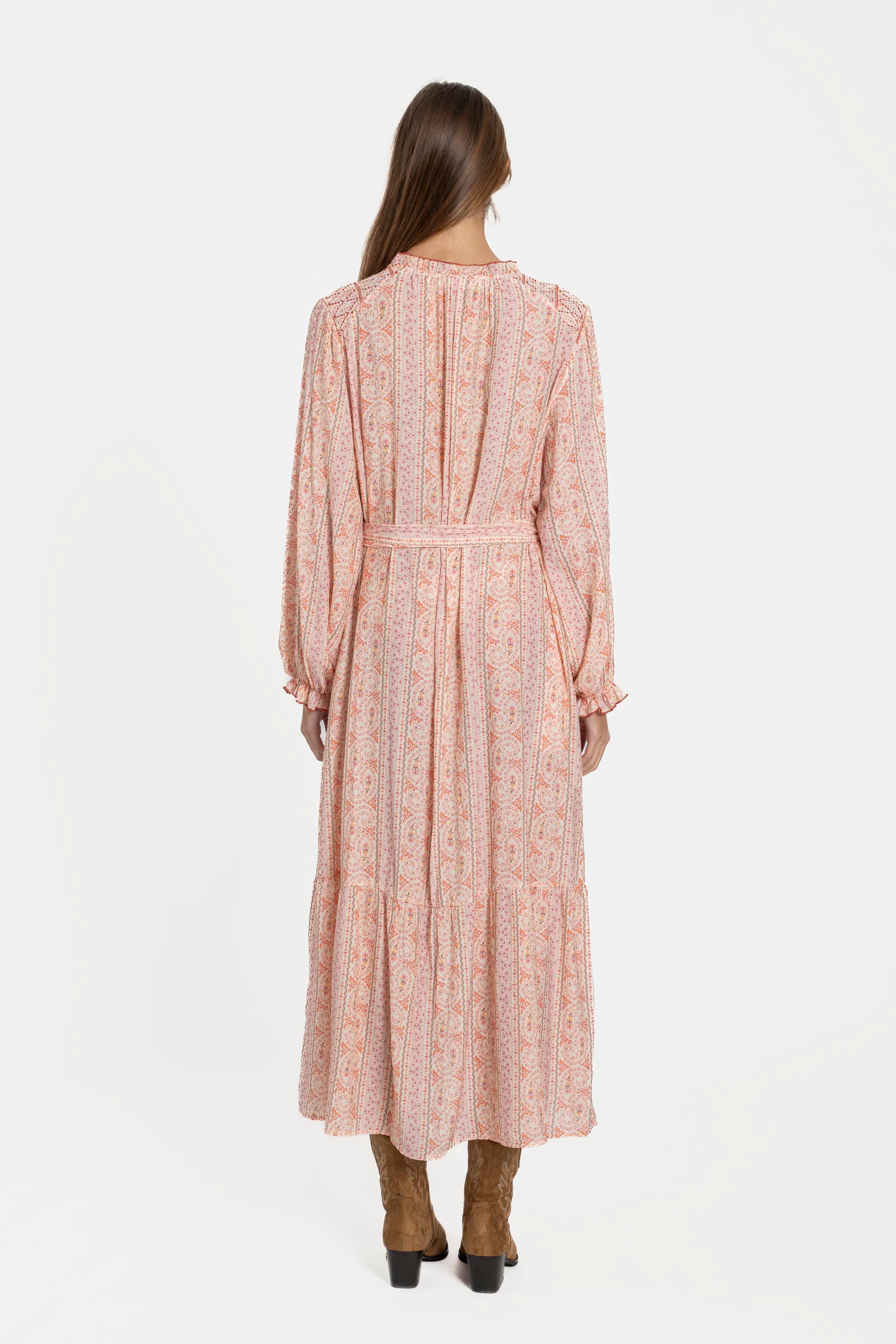 Vue arrière d'une femme dans une robe longue fluide imprimée avec ceinture rose, soulignant sa coupe fluide et élégante.