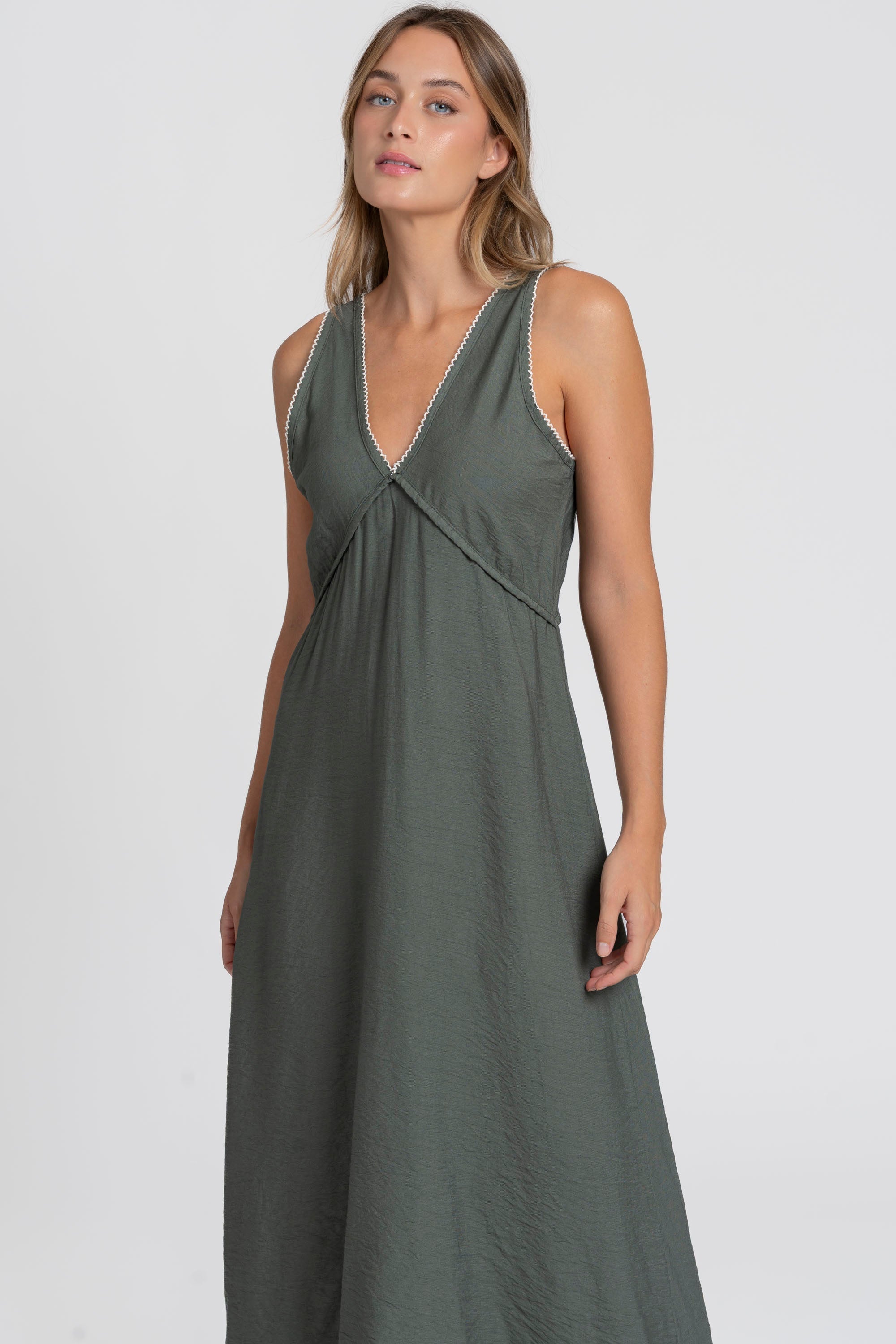 Portrait d'une femme en robe midi fluide brodée en viscose confortable, couleur verte, sous un angle mettant en avant le décolleté.