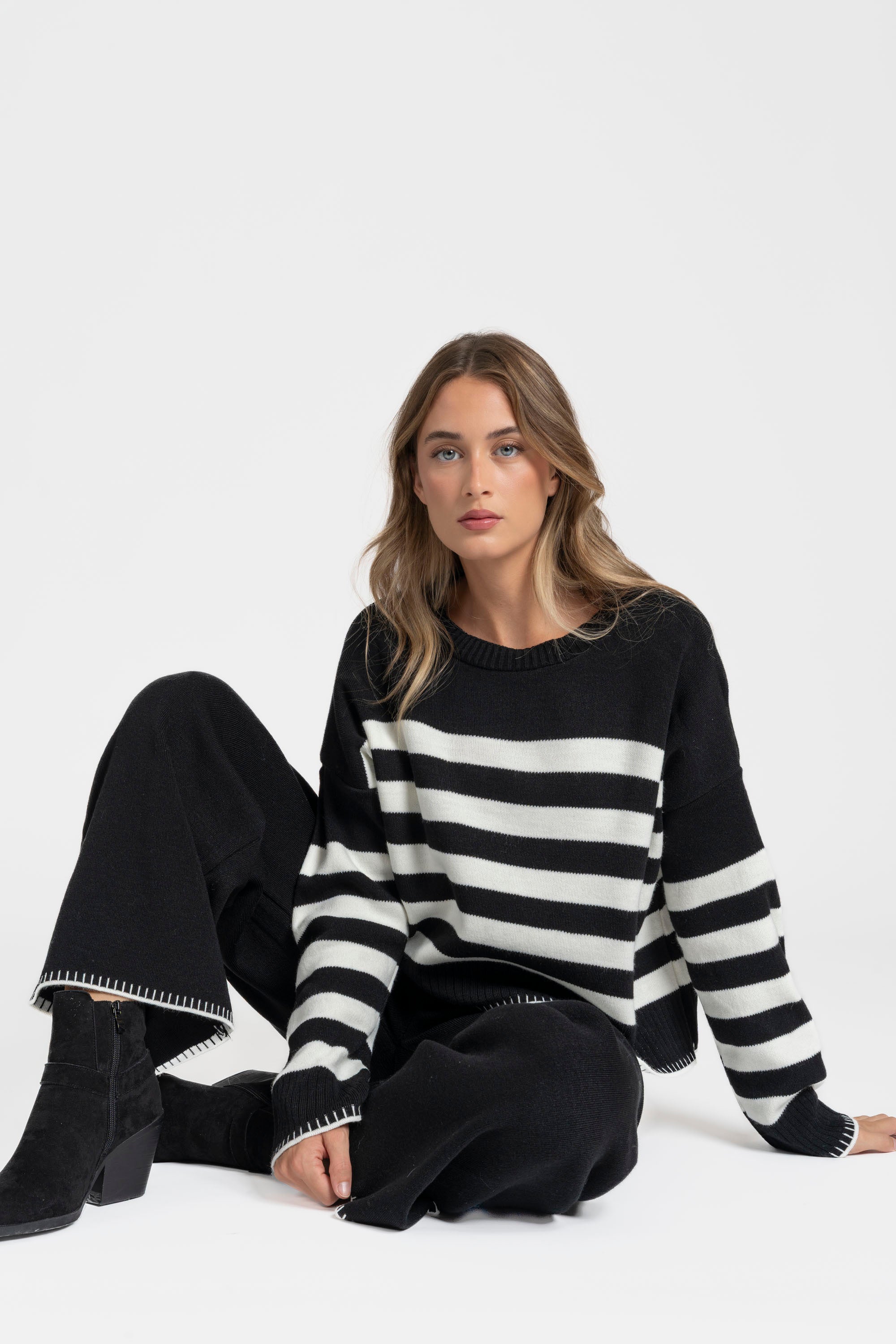 Ensemble maille rayée femme : pull noir à rayures blanches, associé à un pantalon large, look chic.