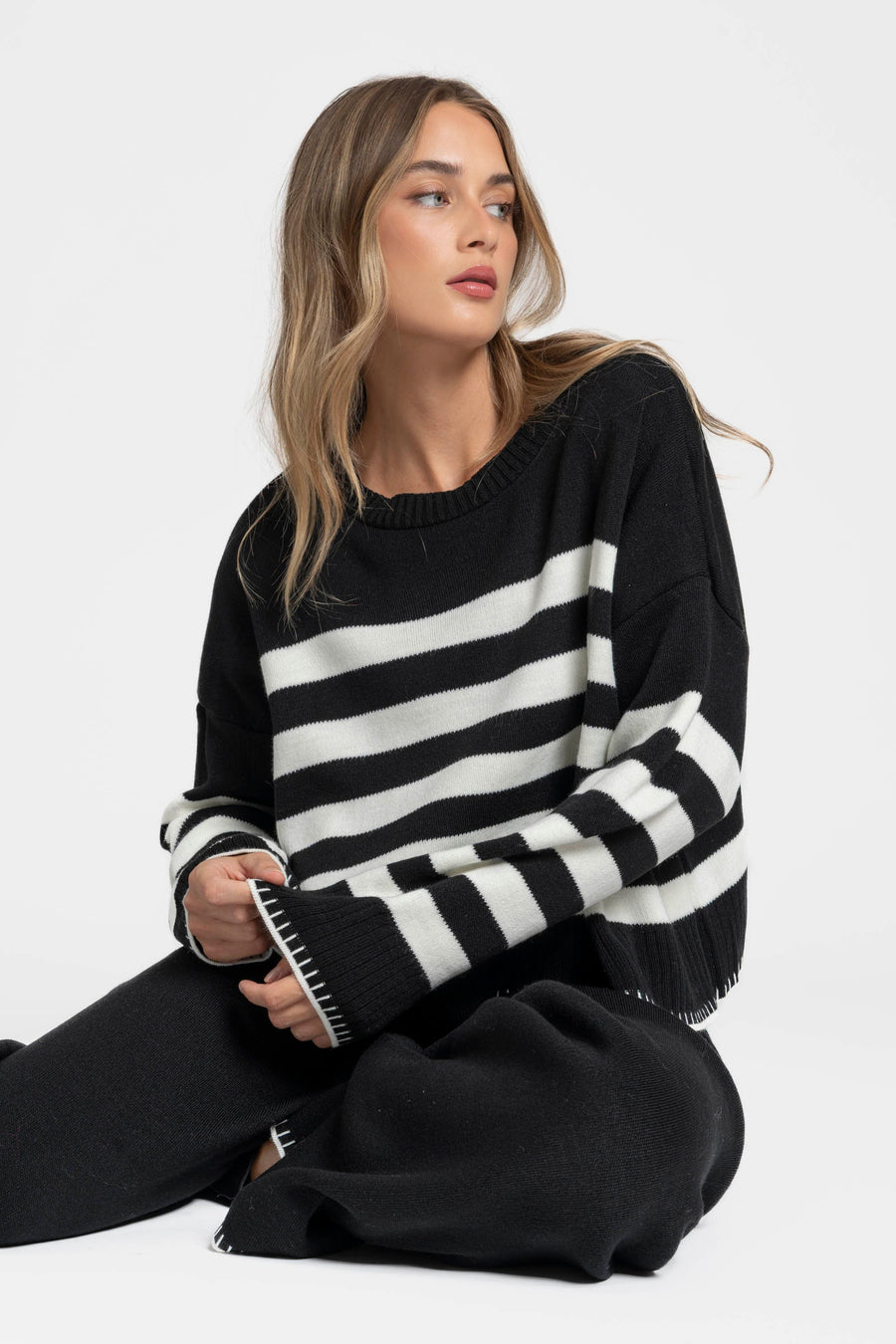 Ensemble maille rayée femme : assise, pull noir à rayures blanches, style décontracté parfait.