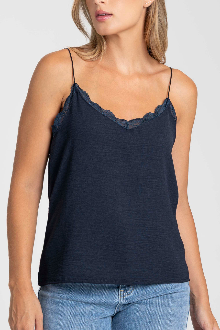 Femme portant le top en mousseline femme fluide à bretelles avec dentelle bleu foncé, en combinaison avec un jean.