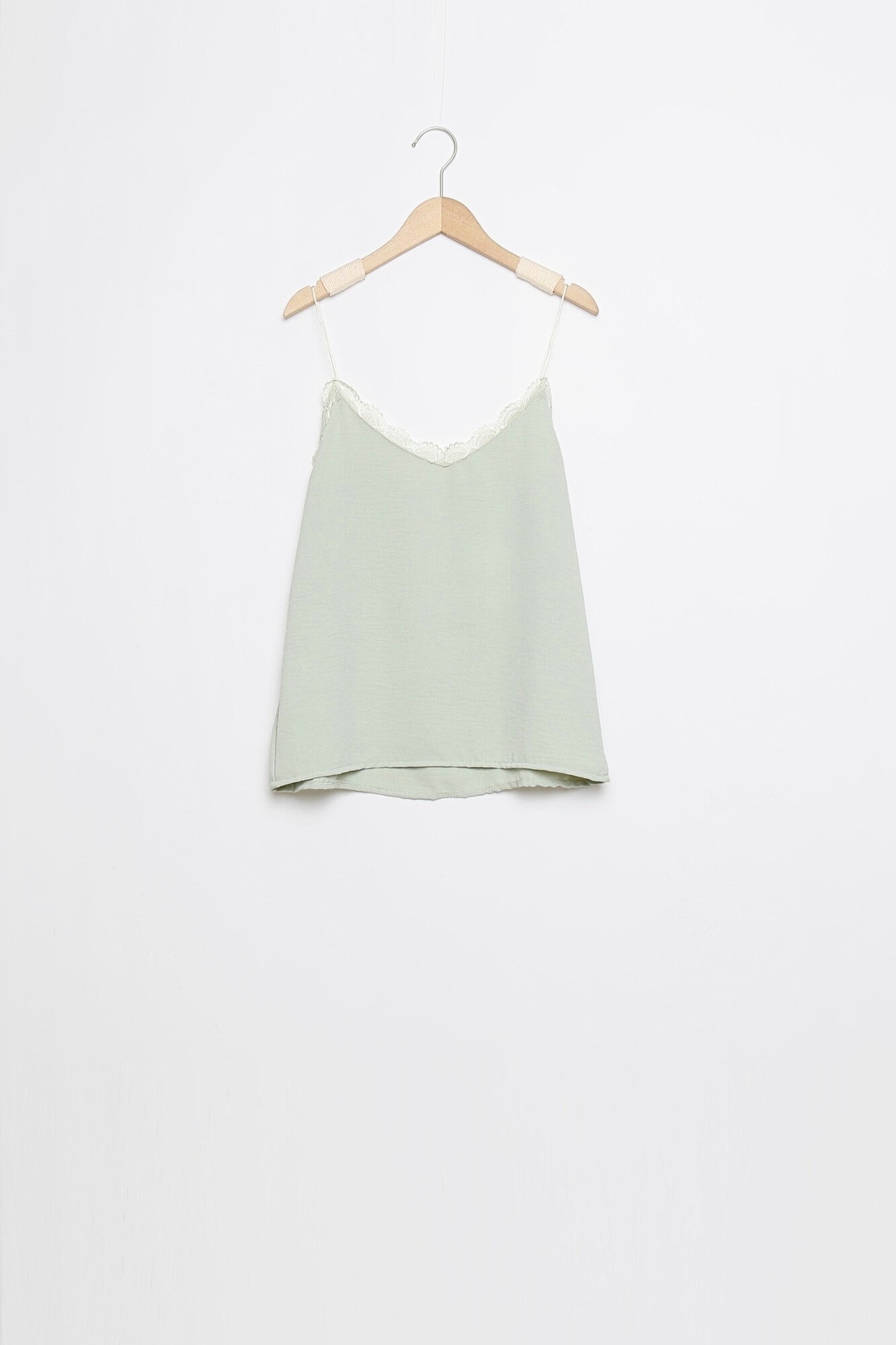 Top en mousseline femme fluide à bretelles avec dentelle vert clair, suspendu pour un aperçu de la coupe.