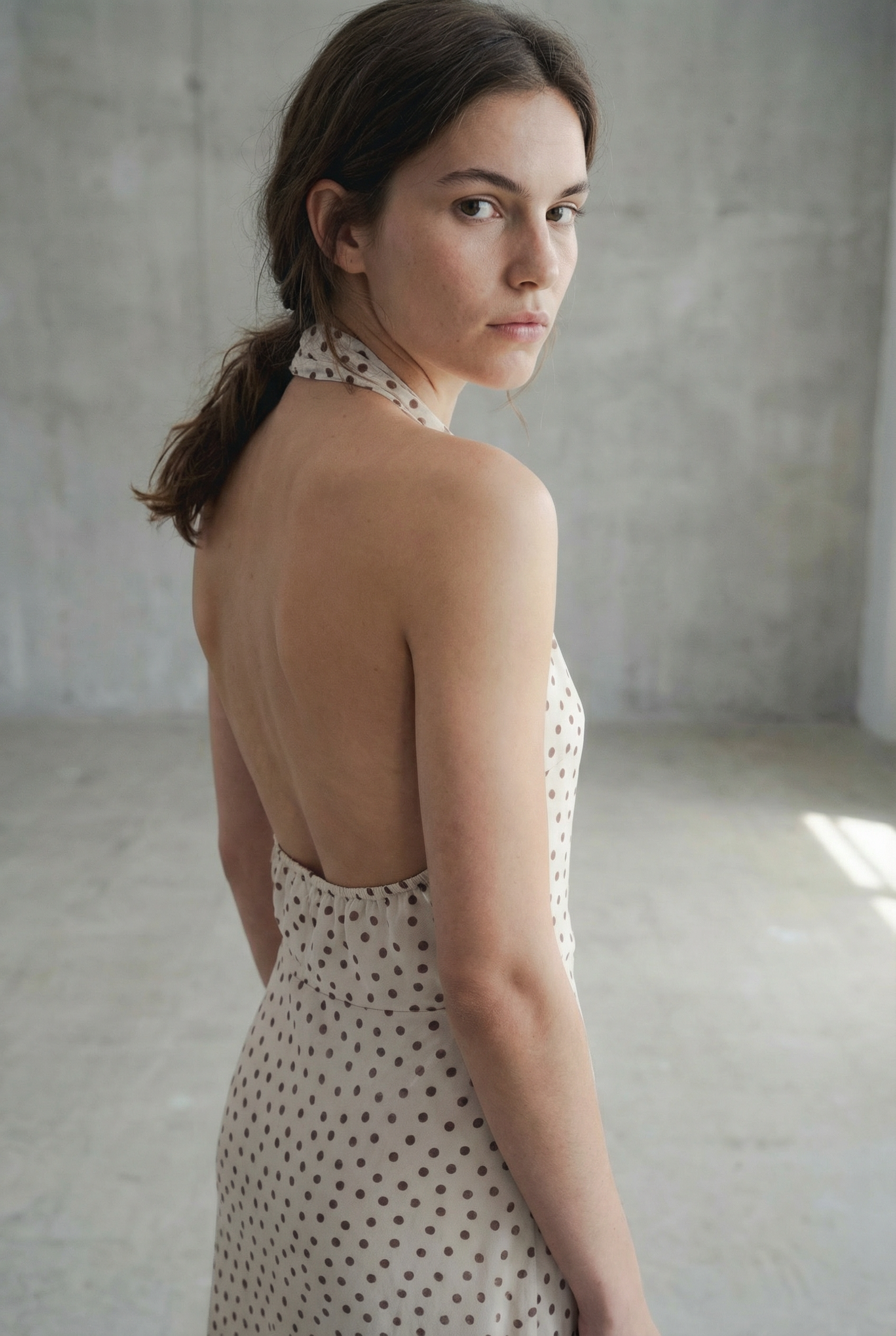 Vue arrière d'une femme dans une robe midi imprimée écru à pois, col halter décolleté plongeant, montrant un dos nu.
