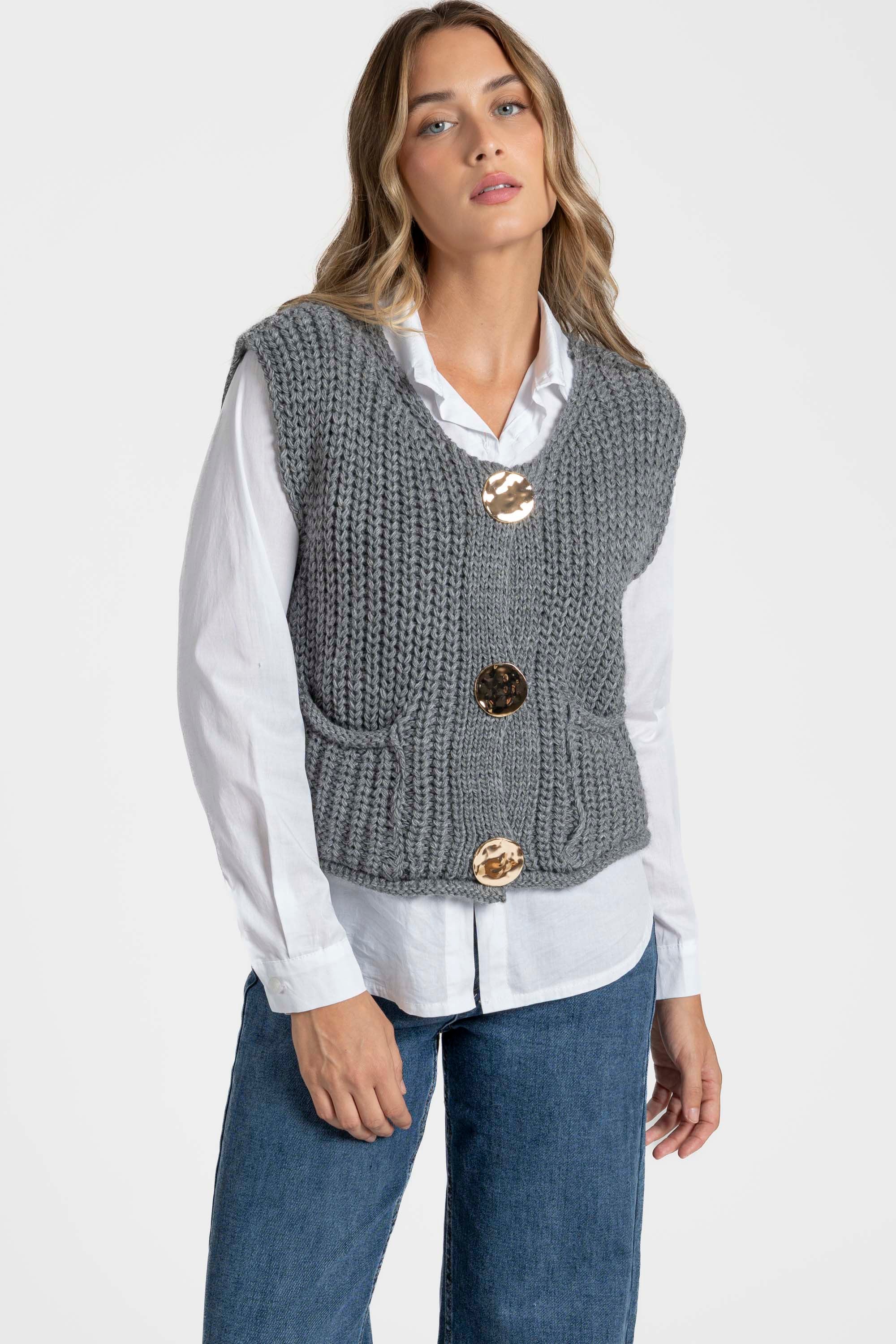 Femme avec un gilet sans manches en maille femme gris, portant une chemise blanche en dessous, mettant en avant des boutons métalliques et des poches. Gilet maille femme.